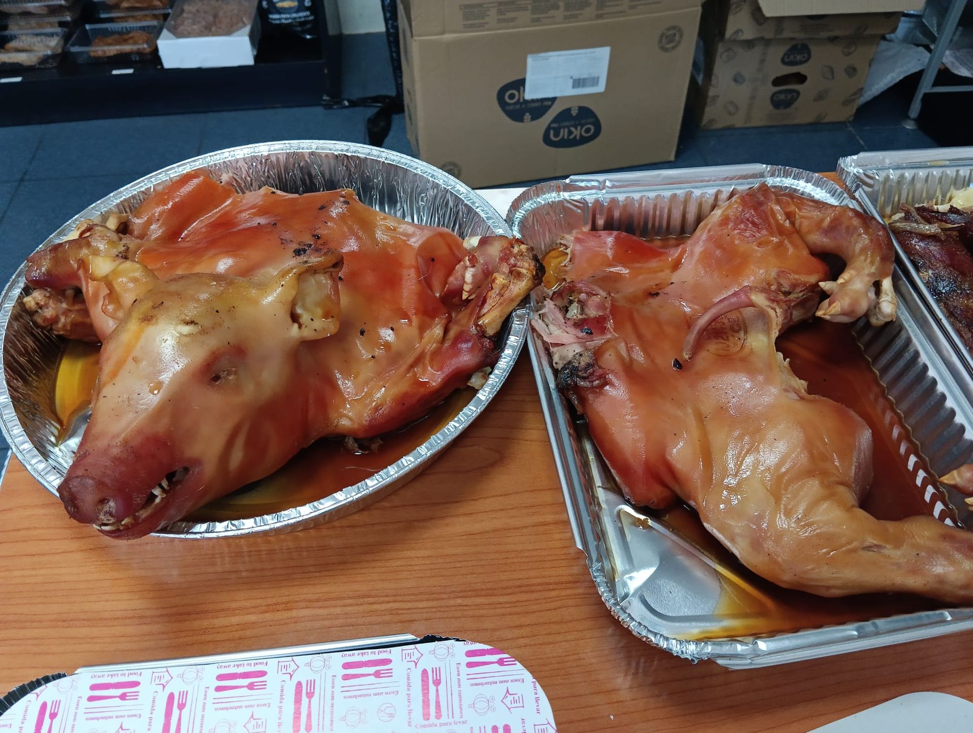 Dos cabezas de cerdo asadas en bandejas de aluminio sobre una mesa.