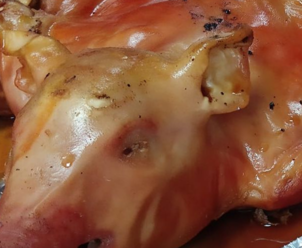 Primer plano de una cabeza de cerdo asada. Piel rosada con algo de carbón oscuro. Orejas y cuencas oculares visibles.