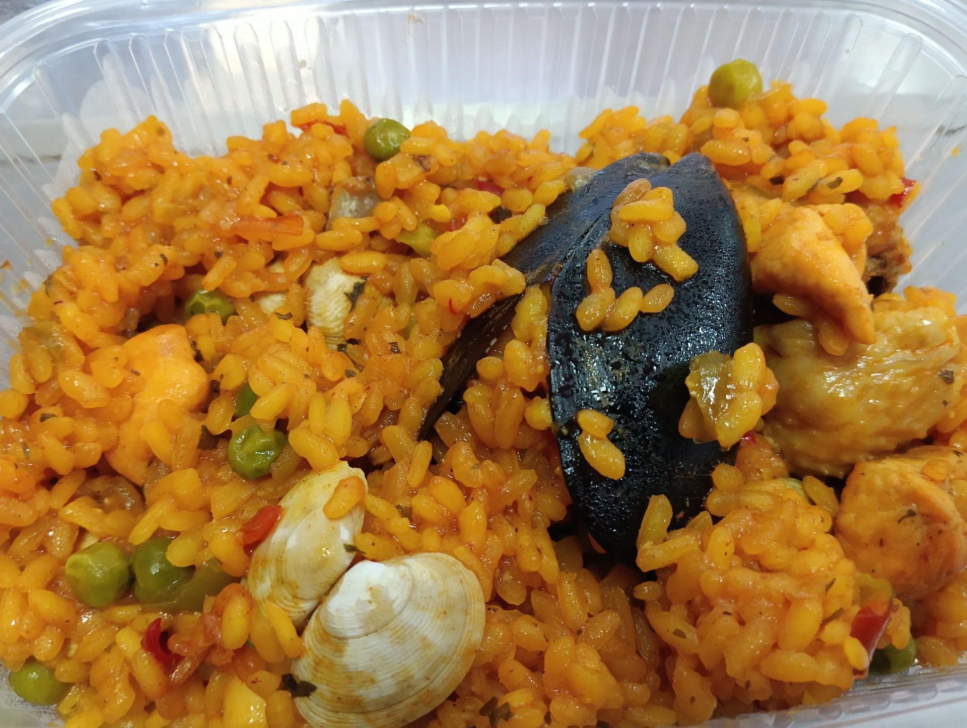 Plato de arroz en paella con marisco (mejillones), verduras y colorante naranja en recipiente de plástico.