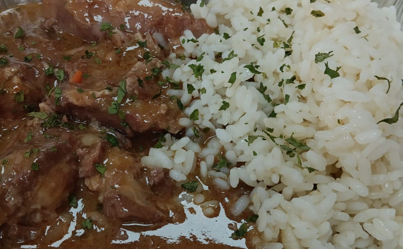 Carne guisada en salsa sobre una cama de arroz blanco, espolvoreada con hierbas.