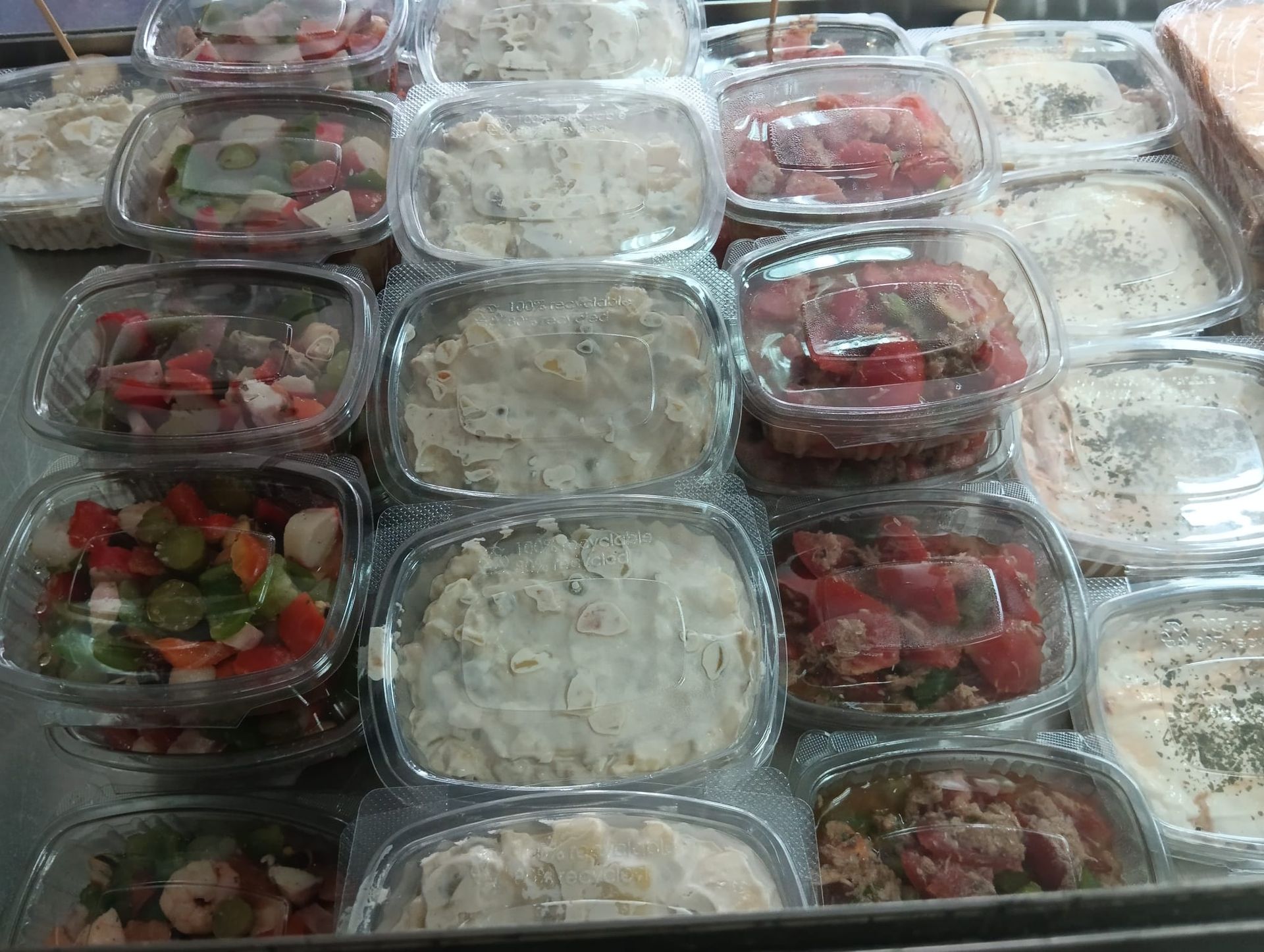 Vitrina con diversas ensaladas preparadas en envases de plástico transparente.