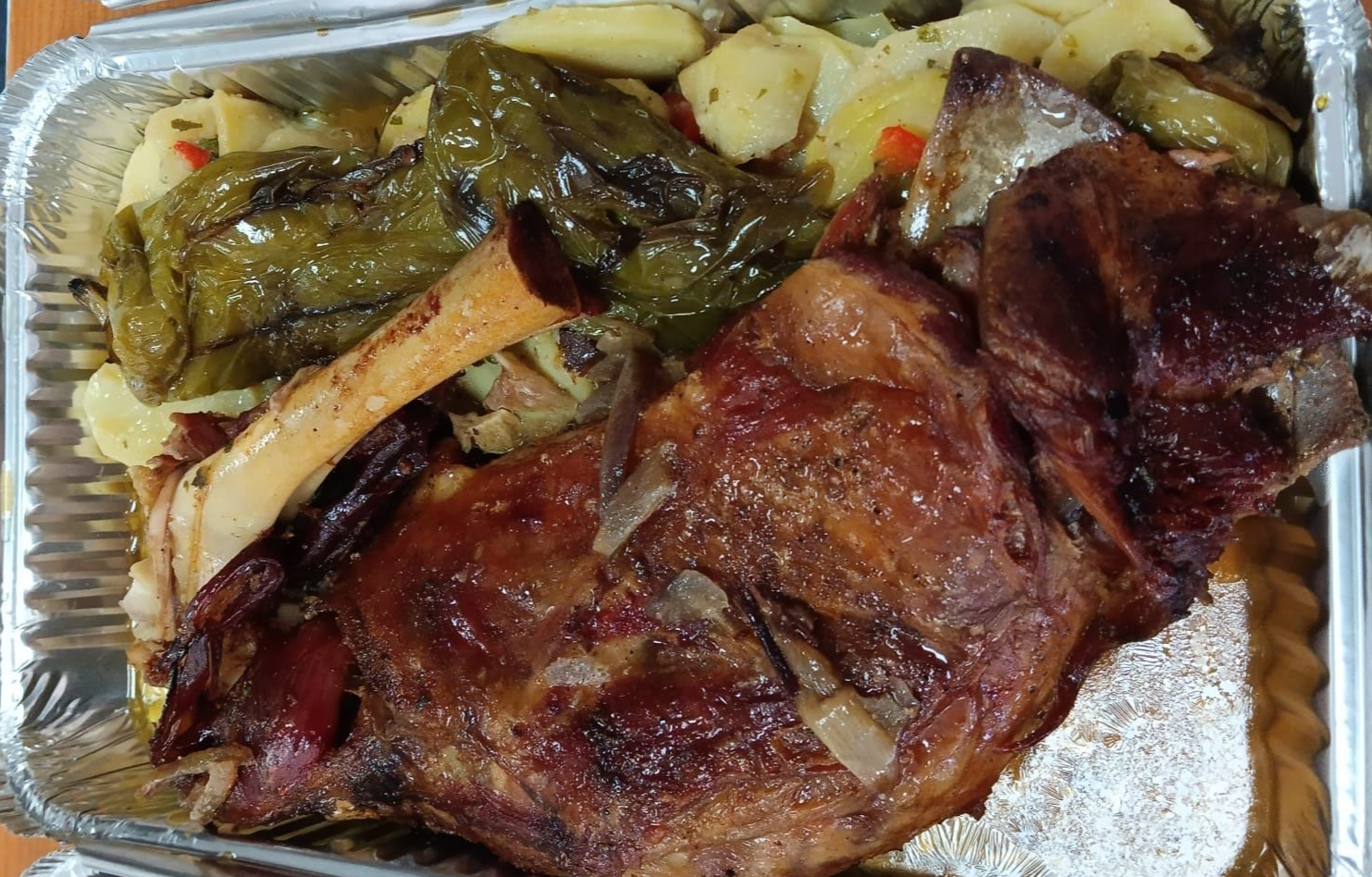 Pierna de cordero asada con verduras en recipiente de aluminio.