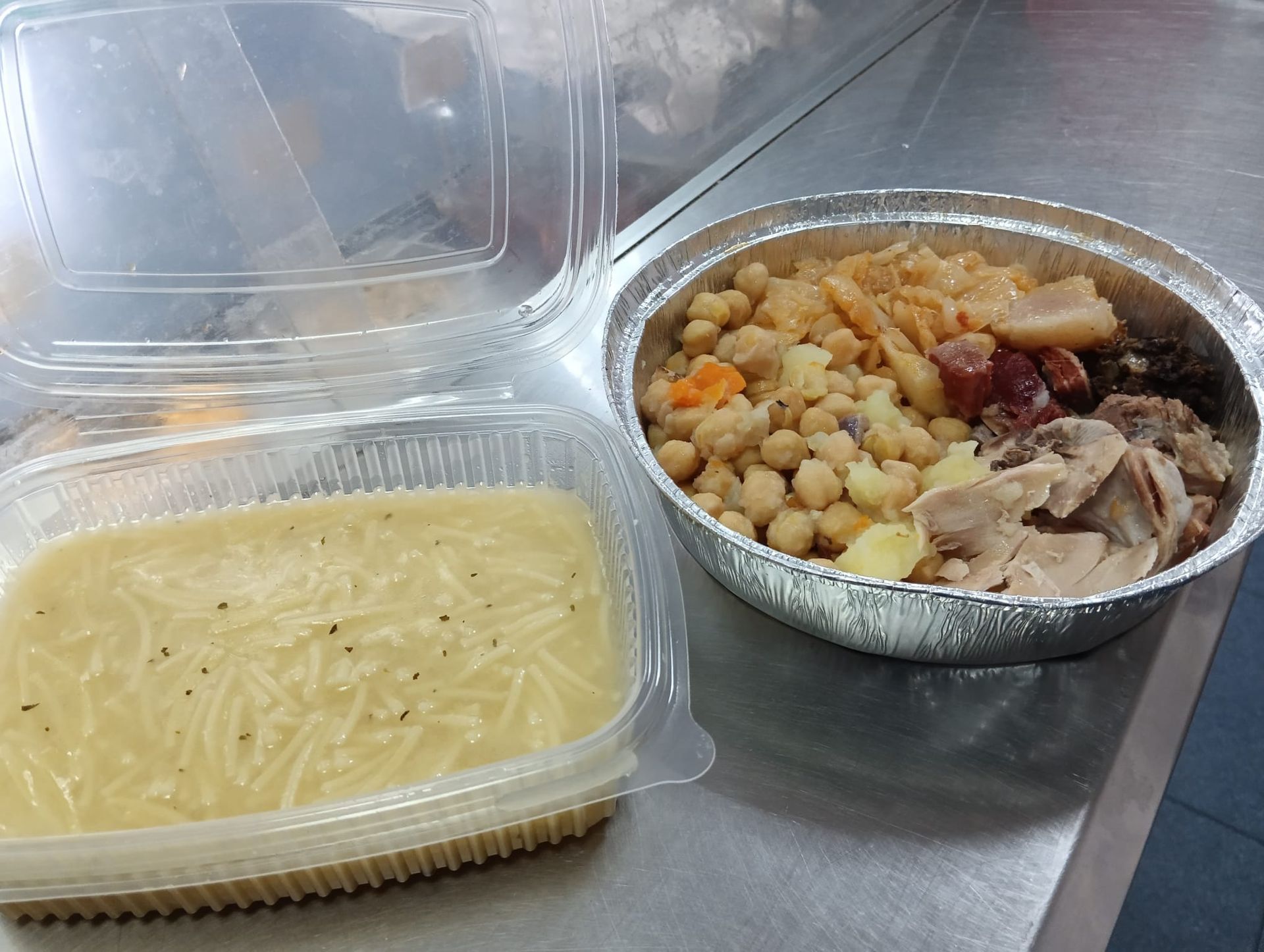 Una comida para llevar con sopa y un guiso de garbanzos, carne y salchichas.