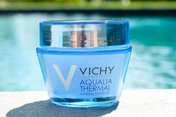 Un frasco de agua mineral termal Vichy Aqualia se encuentra sobre una mesa al lado de una piscina.