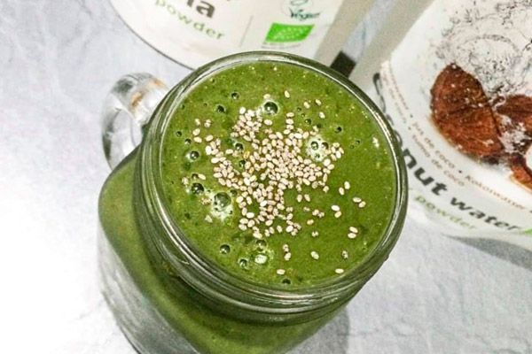 Un batido verde en un frasco de vidrio con semillas de sésamo encima.