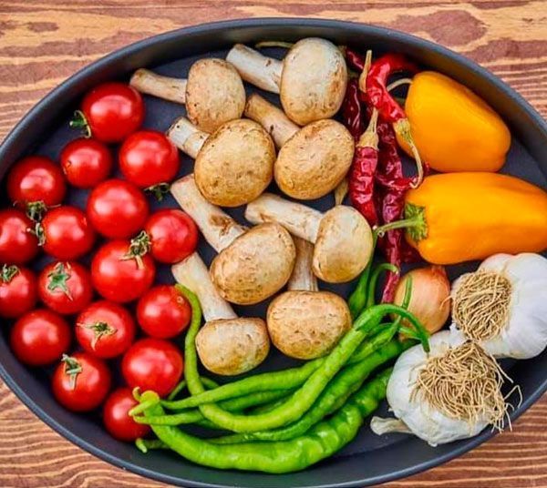 Una sartén llena de tomates, champiñones, pimientos, cebollas y ajo.