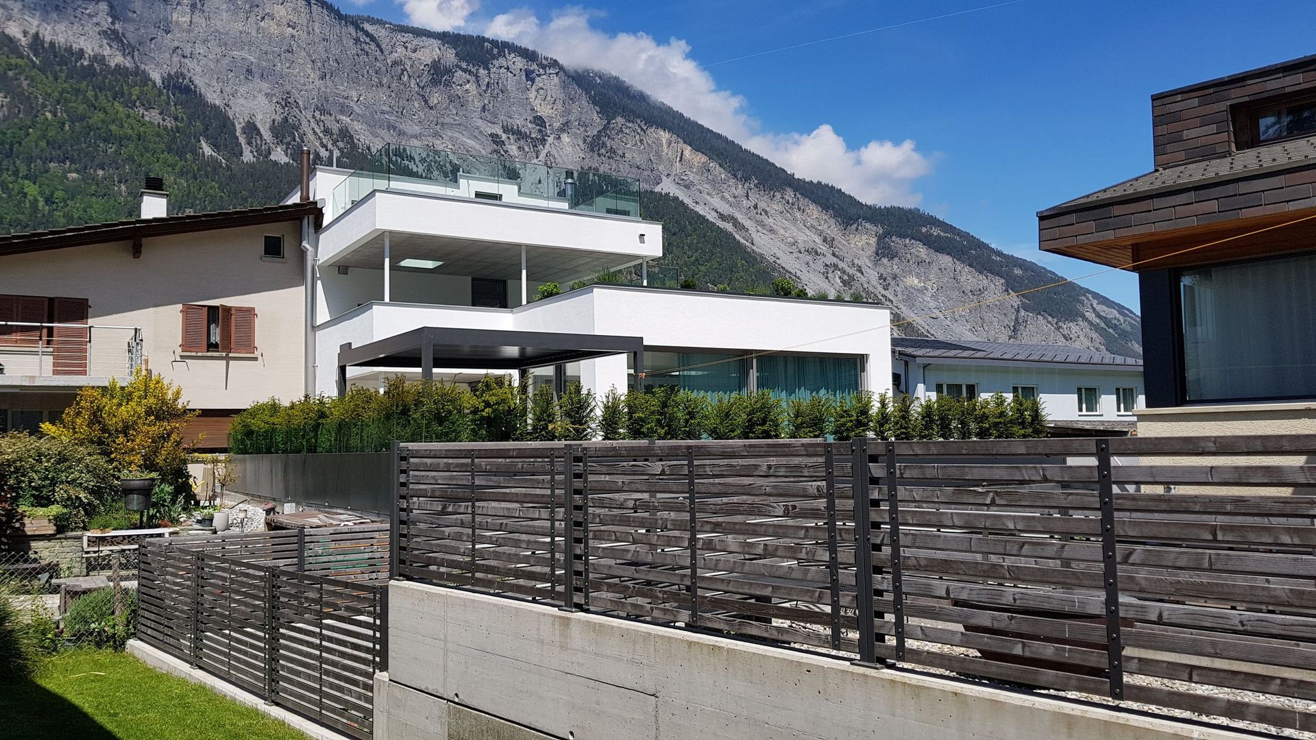 Ein Haus mit einem Holzzaun davor und Bergen im Hintergrund.