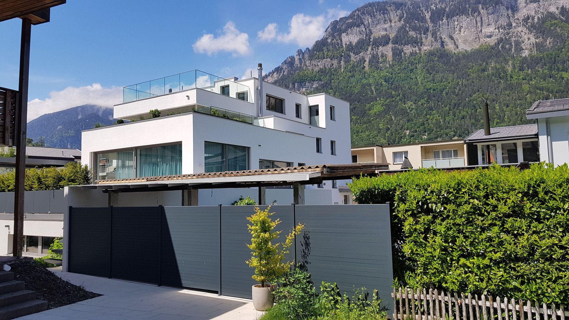 Ein großes weißes Haus mit einem Zaun davor und Bergen im Hintergrund.