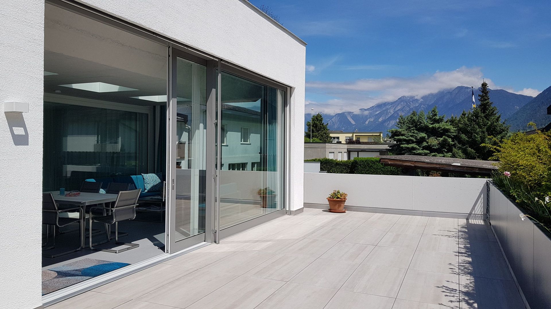 Ein Balkon mit einem Tisch und Stühlen vor einem Gebäude mit Bergen im Hintergrund.
