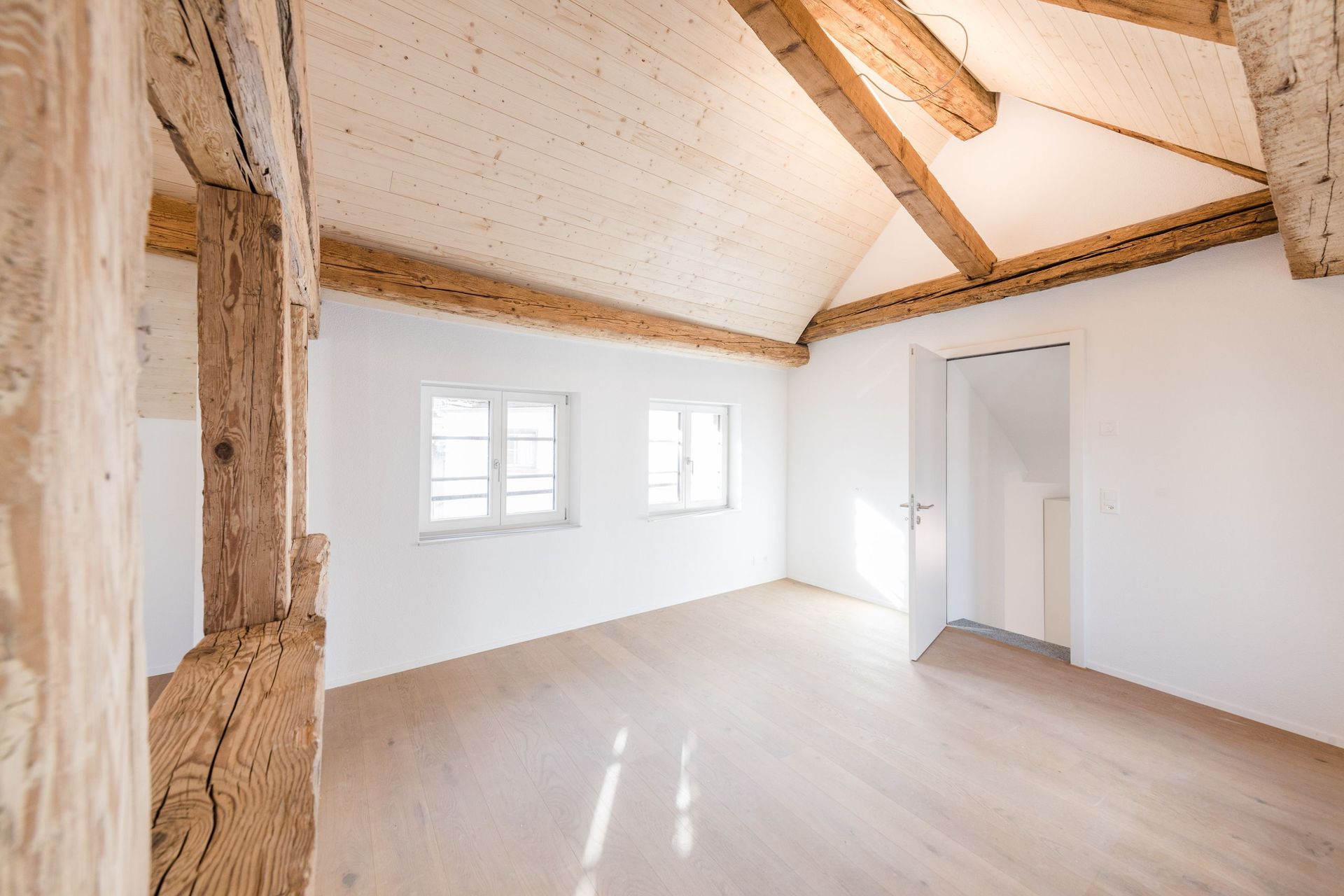 Ein leerer Raum mit Holzbalken und weißen Wänden.