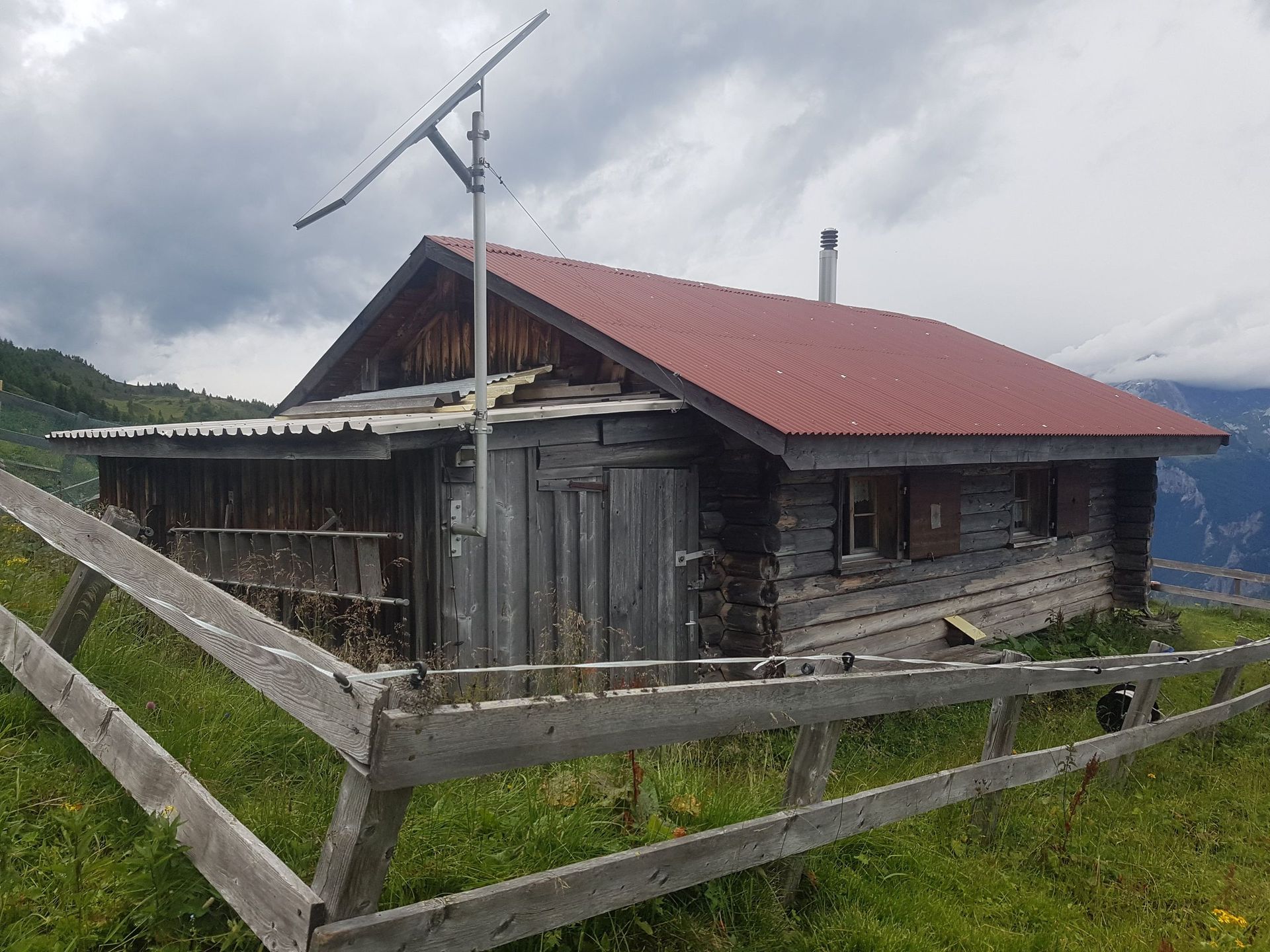 Hinter einem Holzzaun steht ein kleines Holzhaus mit rotem Dach.