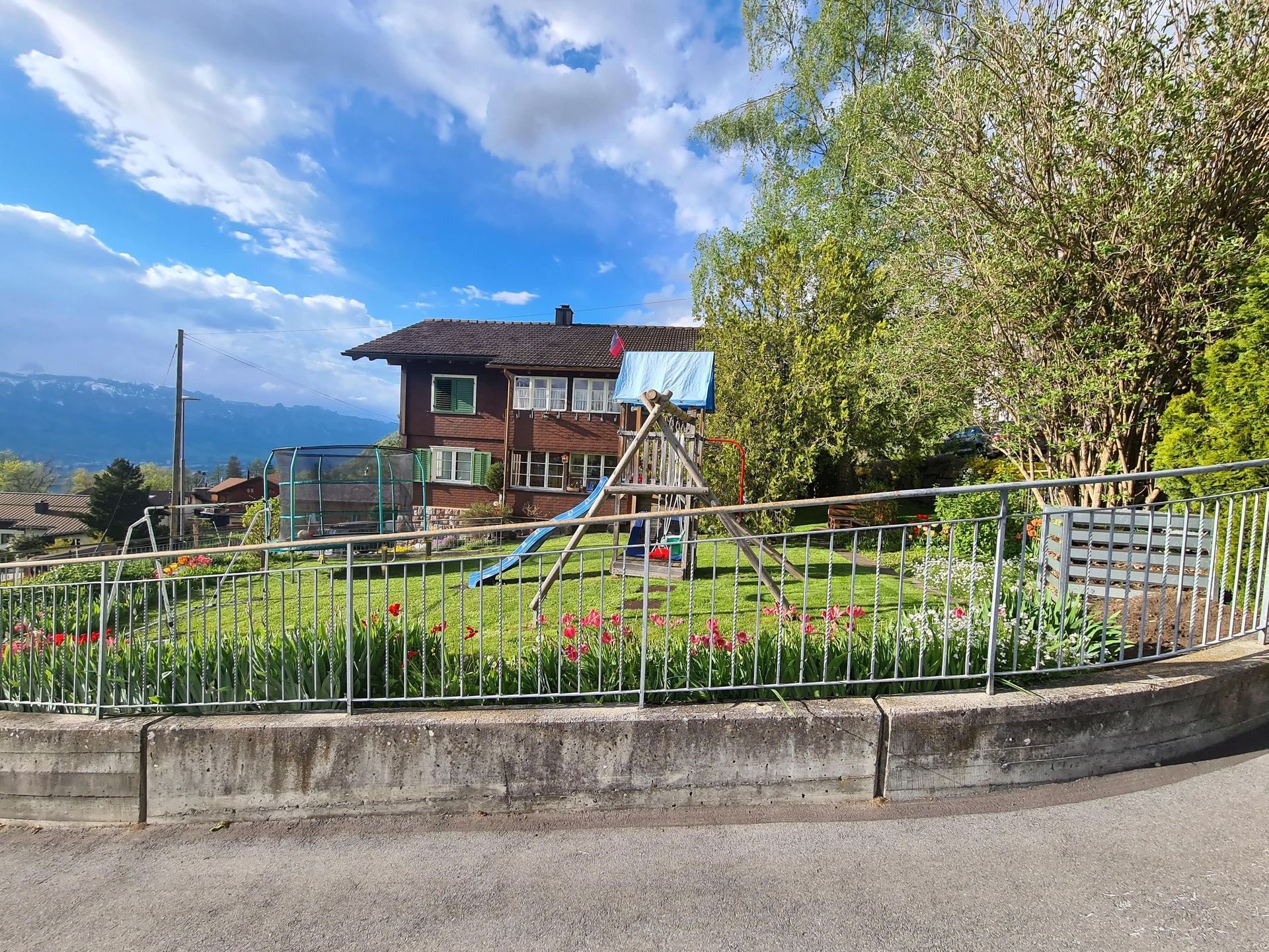 Ein Haus mit einem Spielplatz davor und einem Zaun darum.
