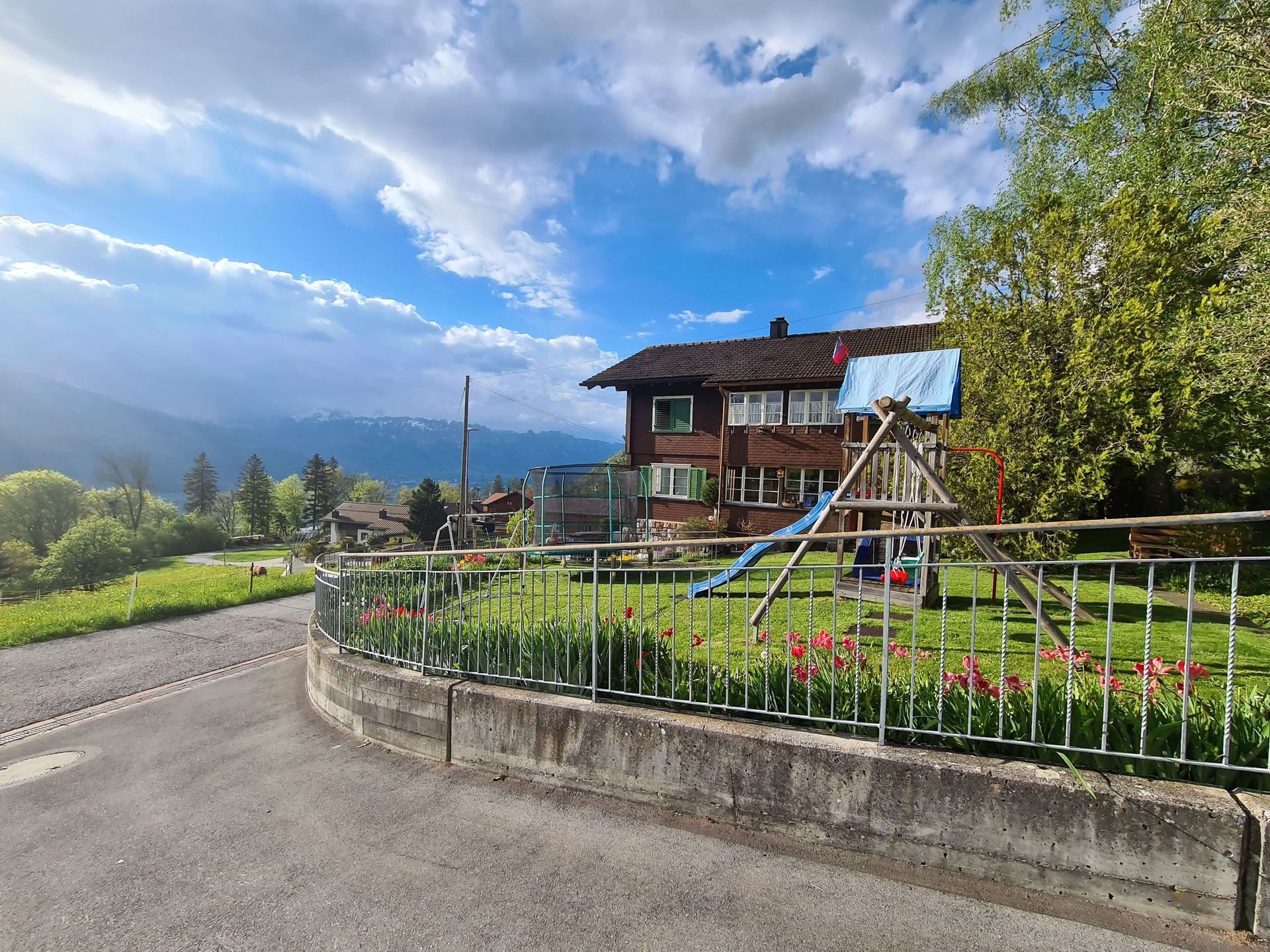 Ein Haus mit einem Spielplatz davor und einem Zaun darum.