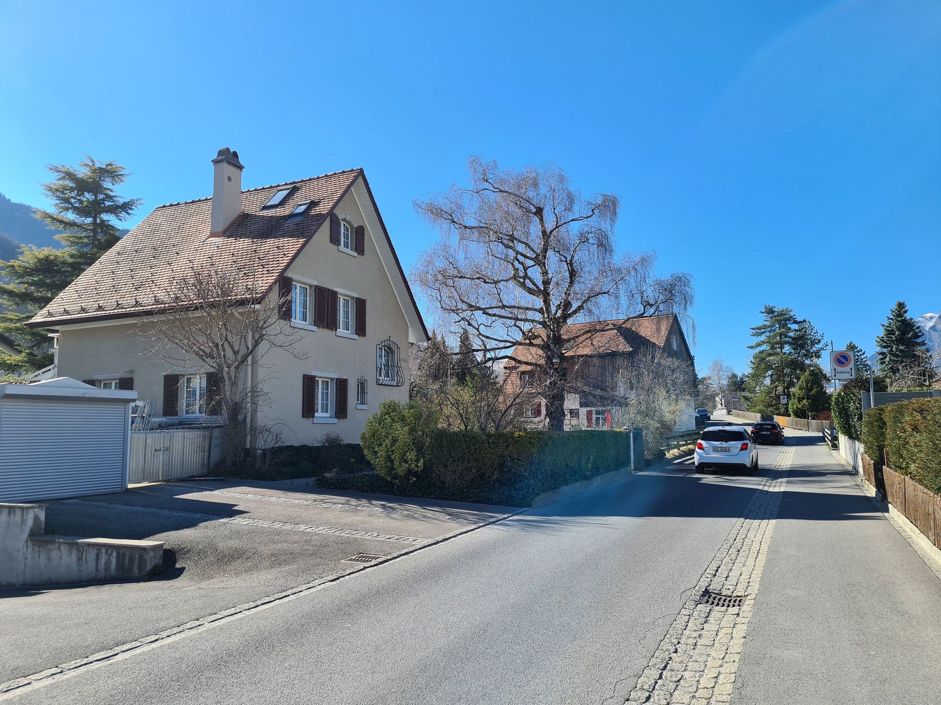 An einem sonnigen Tag fährt ein Auto eine Straße neben einem Haus entlang.