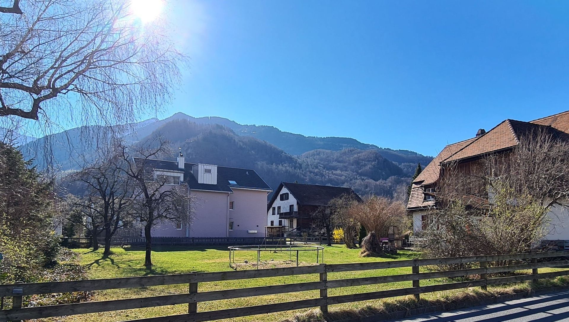Ein Haus mit einem Holzzaun davor und Bergen im Hintergrund.