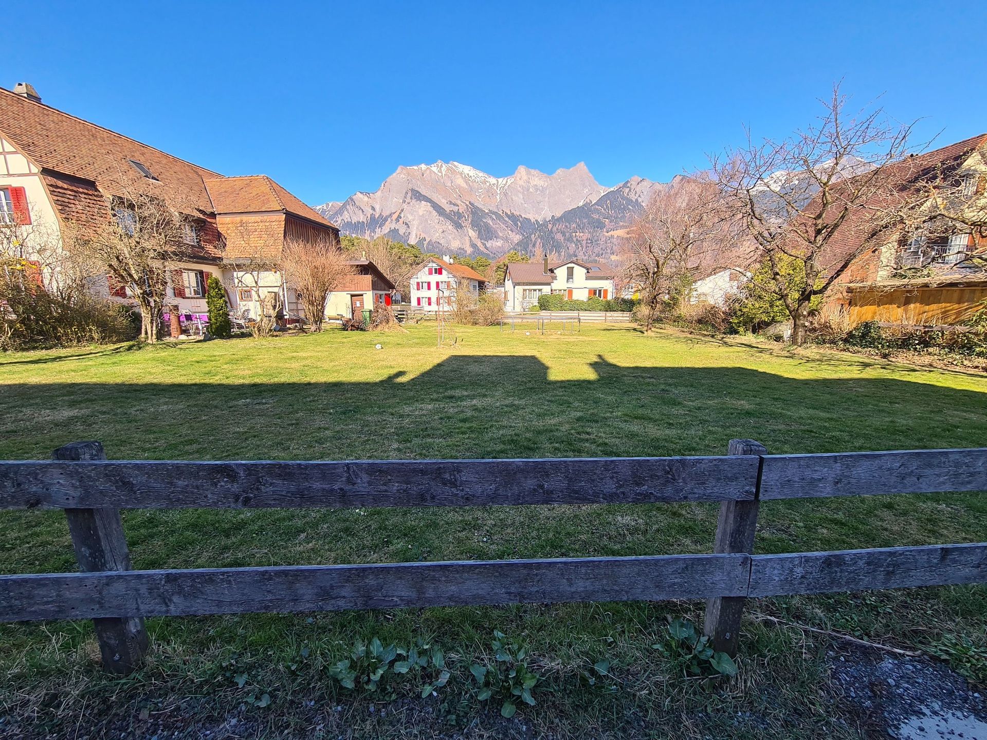 Ein Holzzaun umgibt eine Wiese mit Bergen im Hintergrund.
