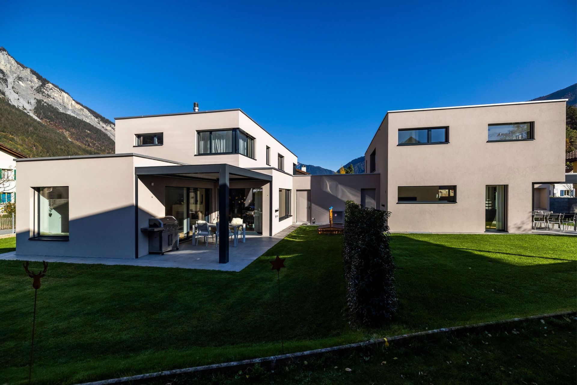 Zwei moderne Häuser liegen nebeneinander auf einem üppig grünen Hügel.