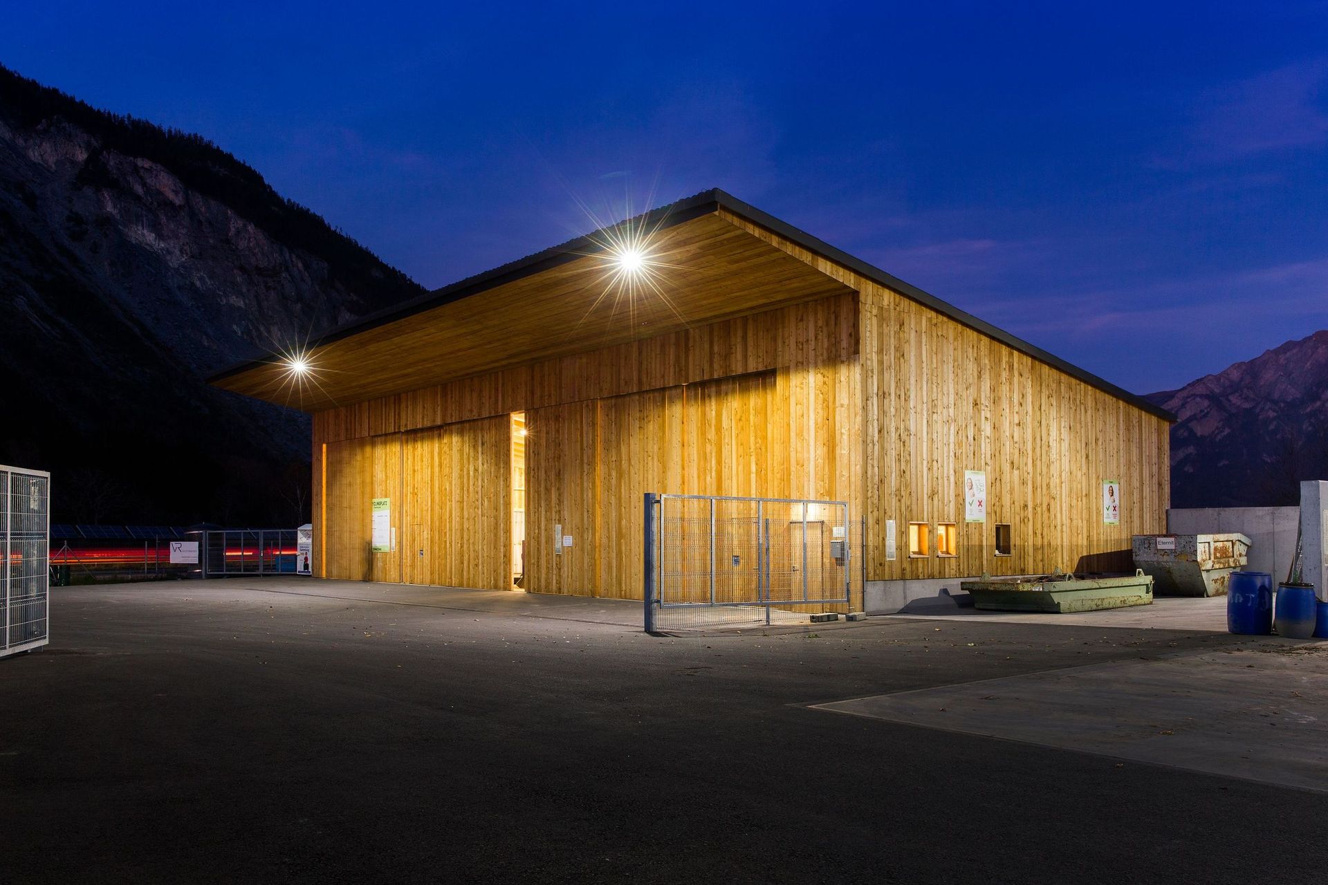 Ein großes Holzgebäude ist nachts beleuchtet, im Hintergrund sind Berge zu sehen.