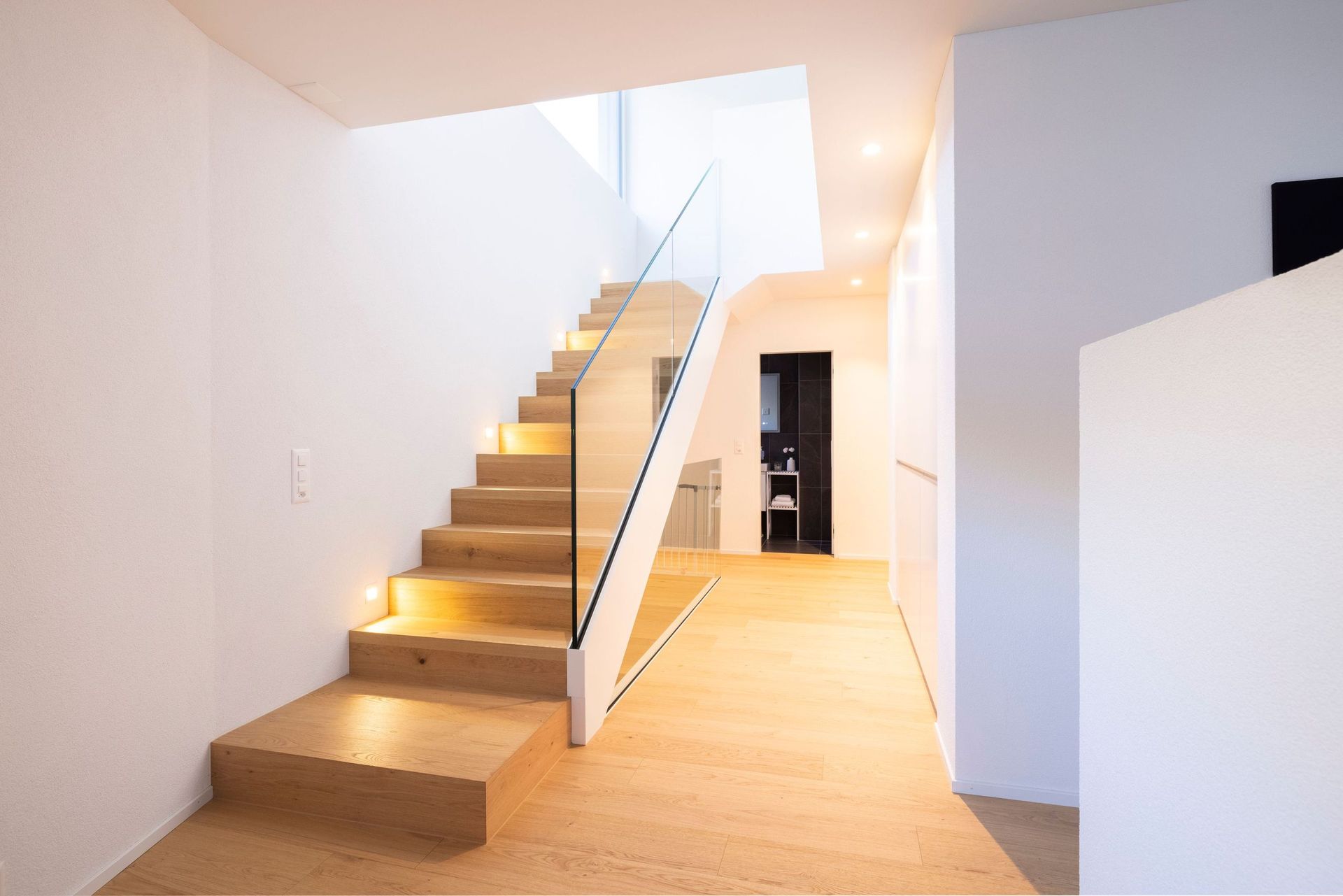 Ein Flur mit einer Holztreppe und einem Glasgeländer.