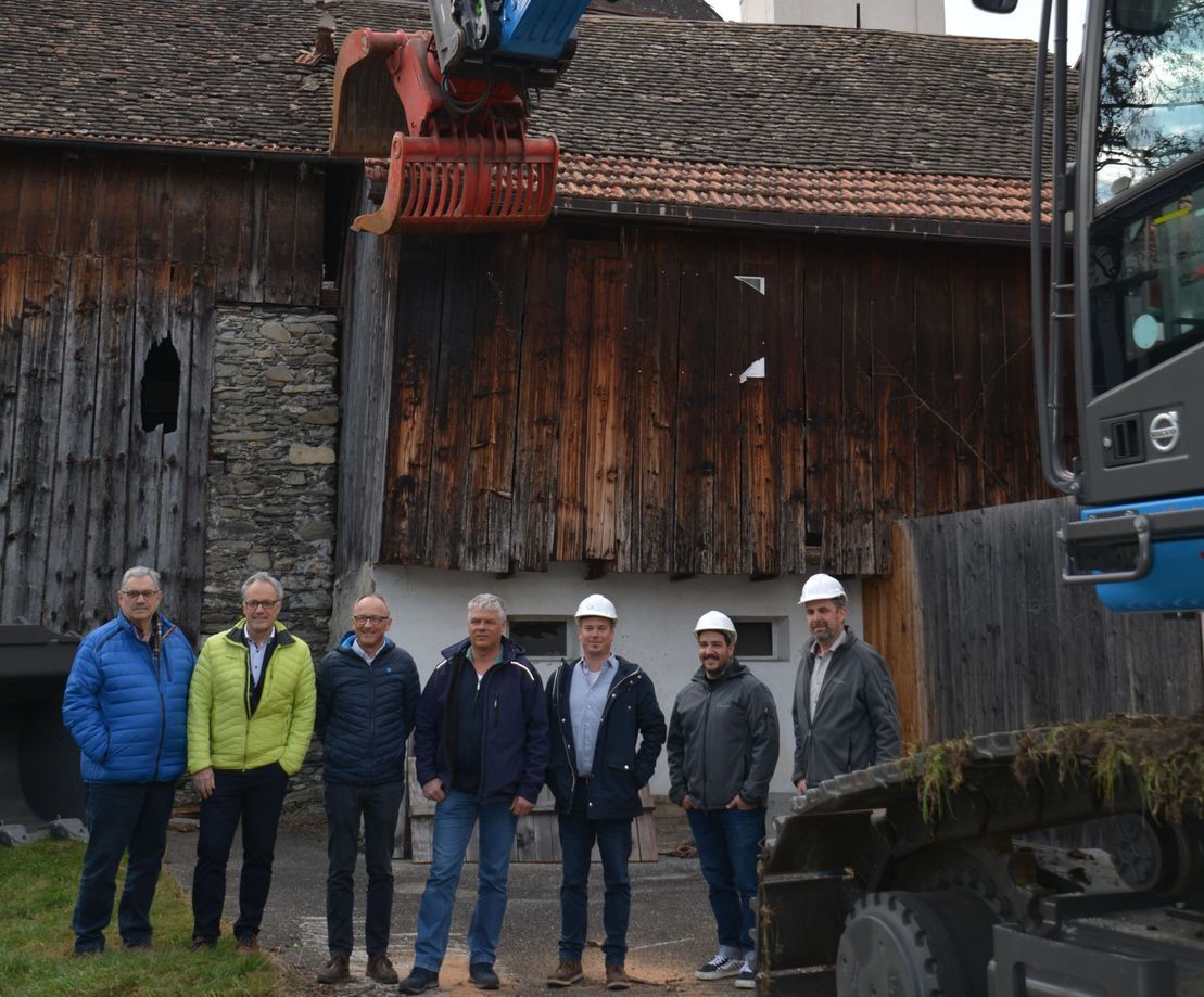 Eine Gruppe Männer steht vor einem Gebäude und einem Baufahrzeug.