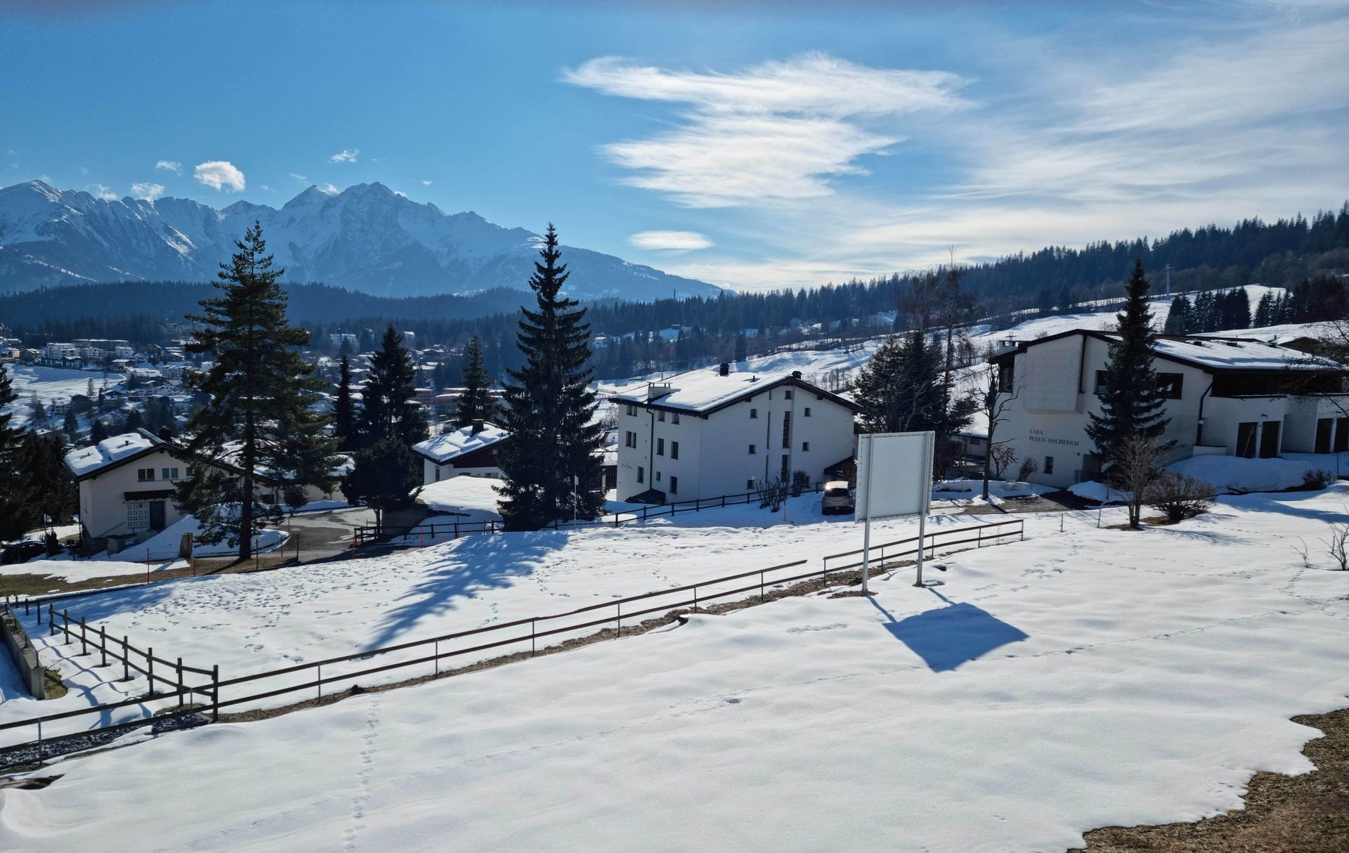 Eine verschneite Landschaft mit Bergen im Hintergrund und Häusern im Vordergrund.