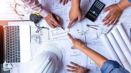 Eine Gruppe von Leuten sitzt um einen Tisch herum und schaut sich einen Bauplan an.