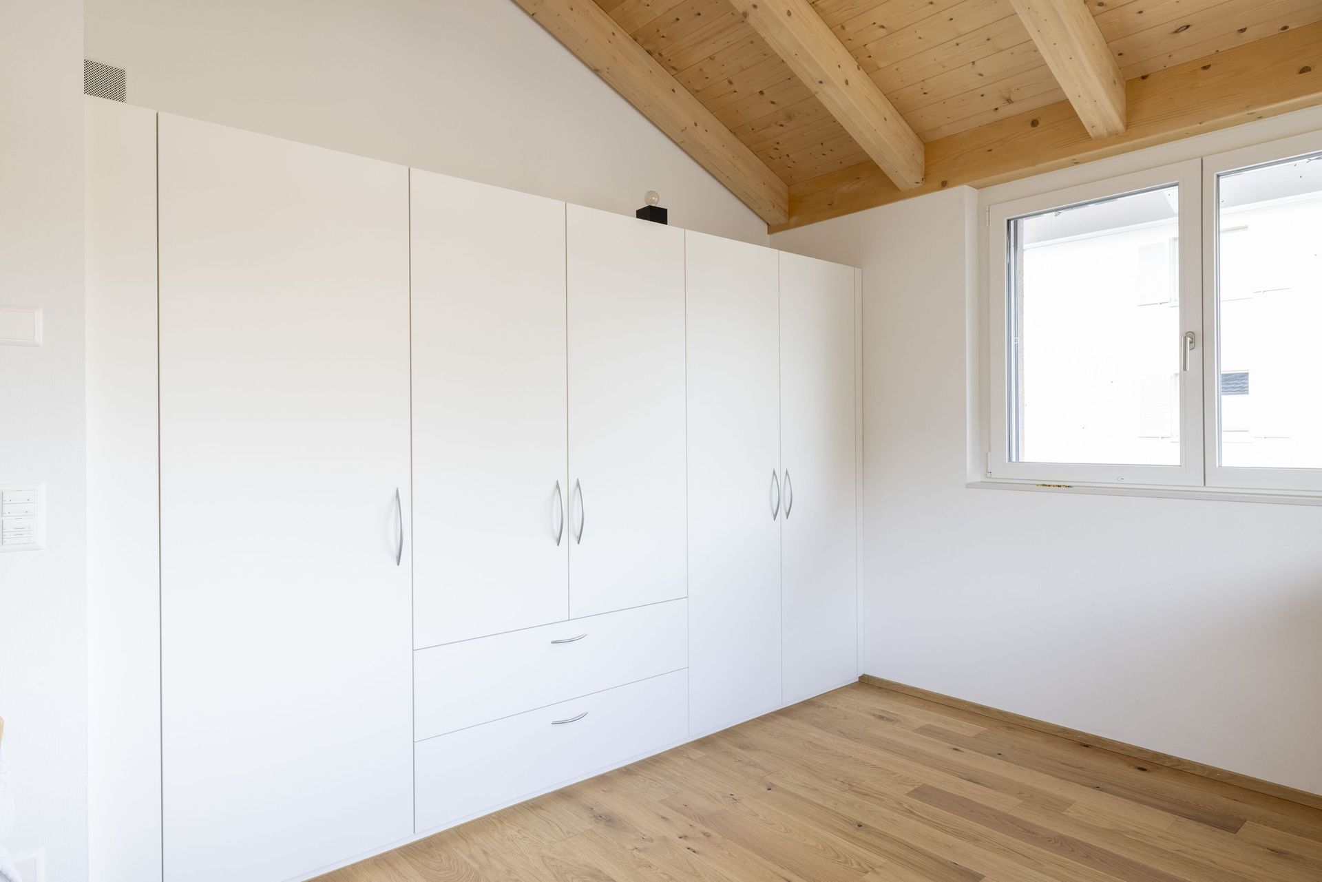 Ein leeres Schlafzimmer mit weißen Schränken und einer Holzdecke.