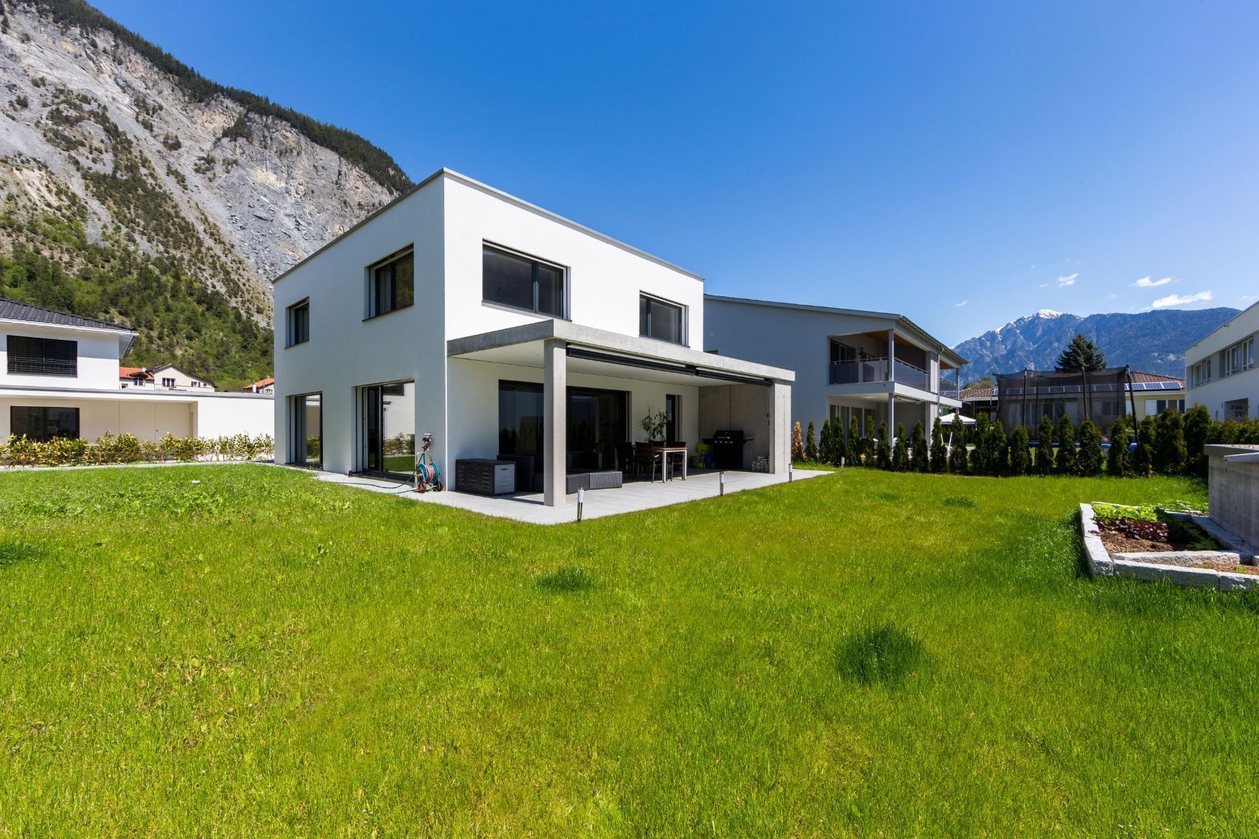 Ein weißes Haus mit einer großen Wiese davor und Bergen im Hintergrund.