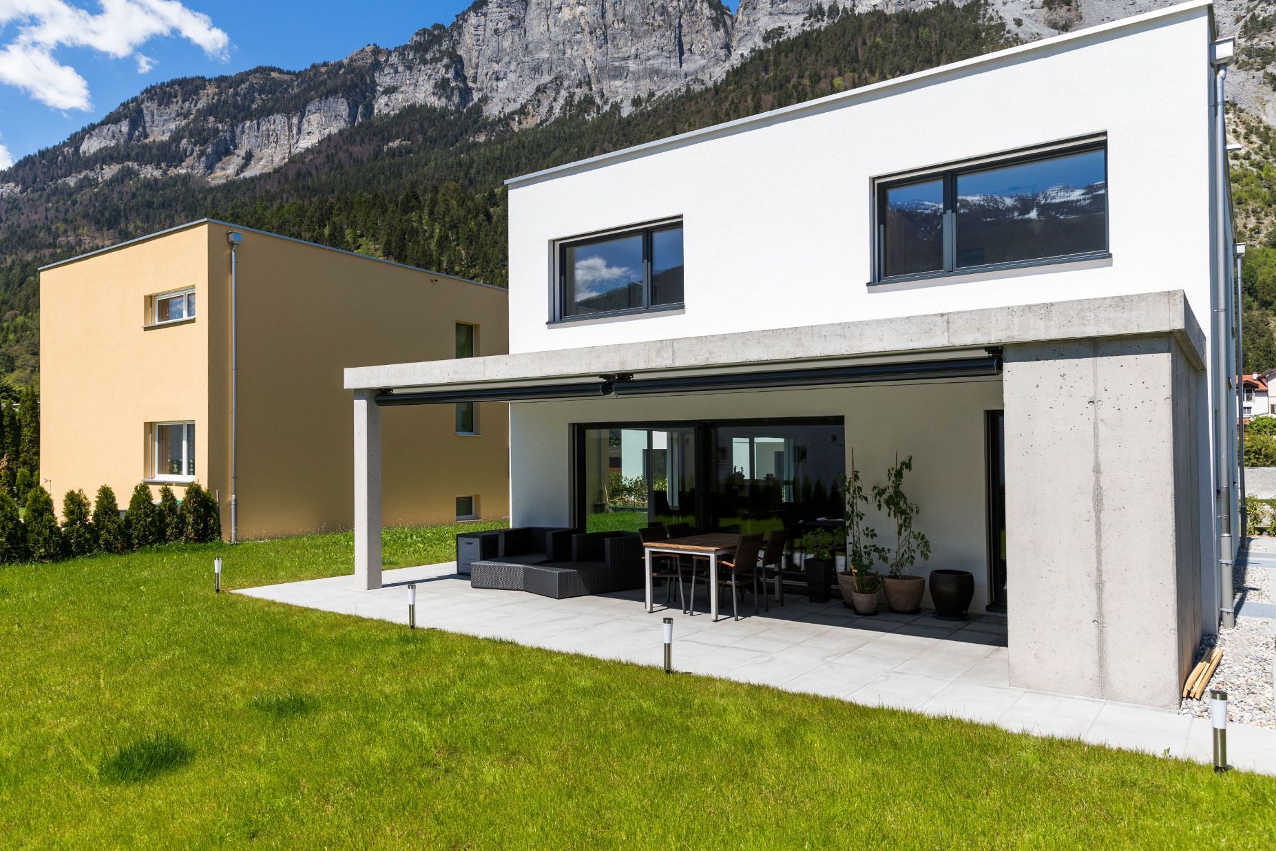 Ein modernes Haus mit einer Terrasse und Bergen im Hintergrund.