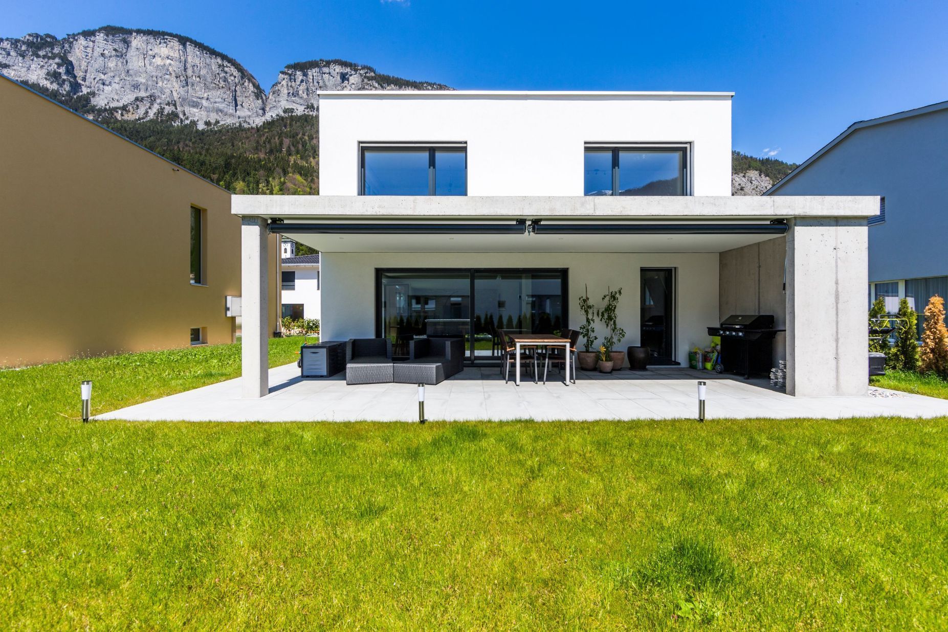 Ein modernes Haus mit einer großen Wiese davor und Bergen im Hintergrund.