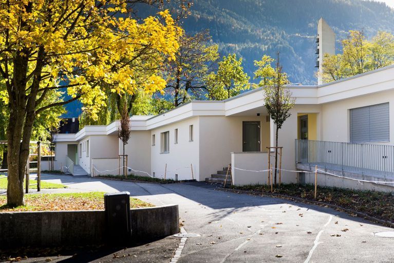 Ein weißes Haus mit gelben Blättern ist von Bäumen und Bergen umgeben.