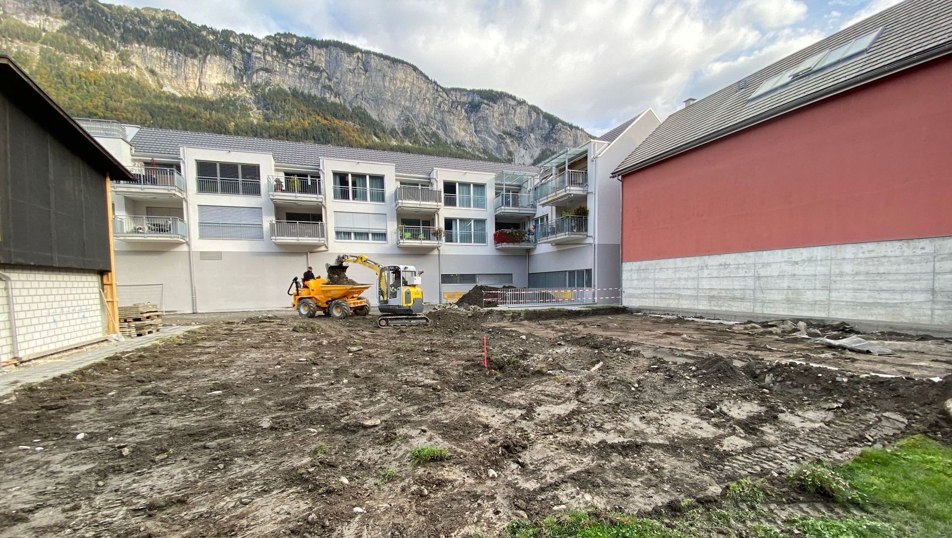 Eine Baustelle mit einem Gebäude im Hintergrund und einem Bulldozer im Vordergrund.