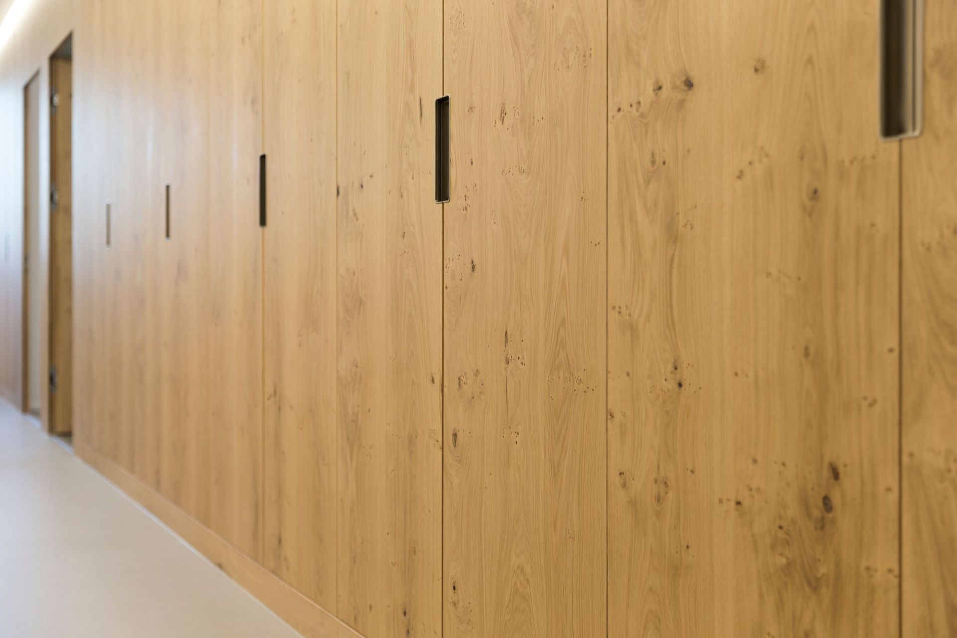 Ein langer Flur mit Holzschränken und schwarzen Griffen.