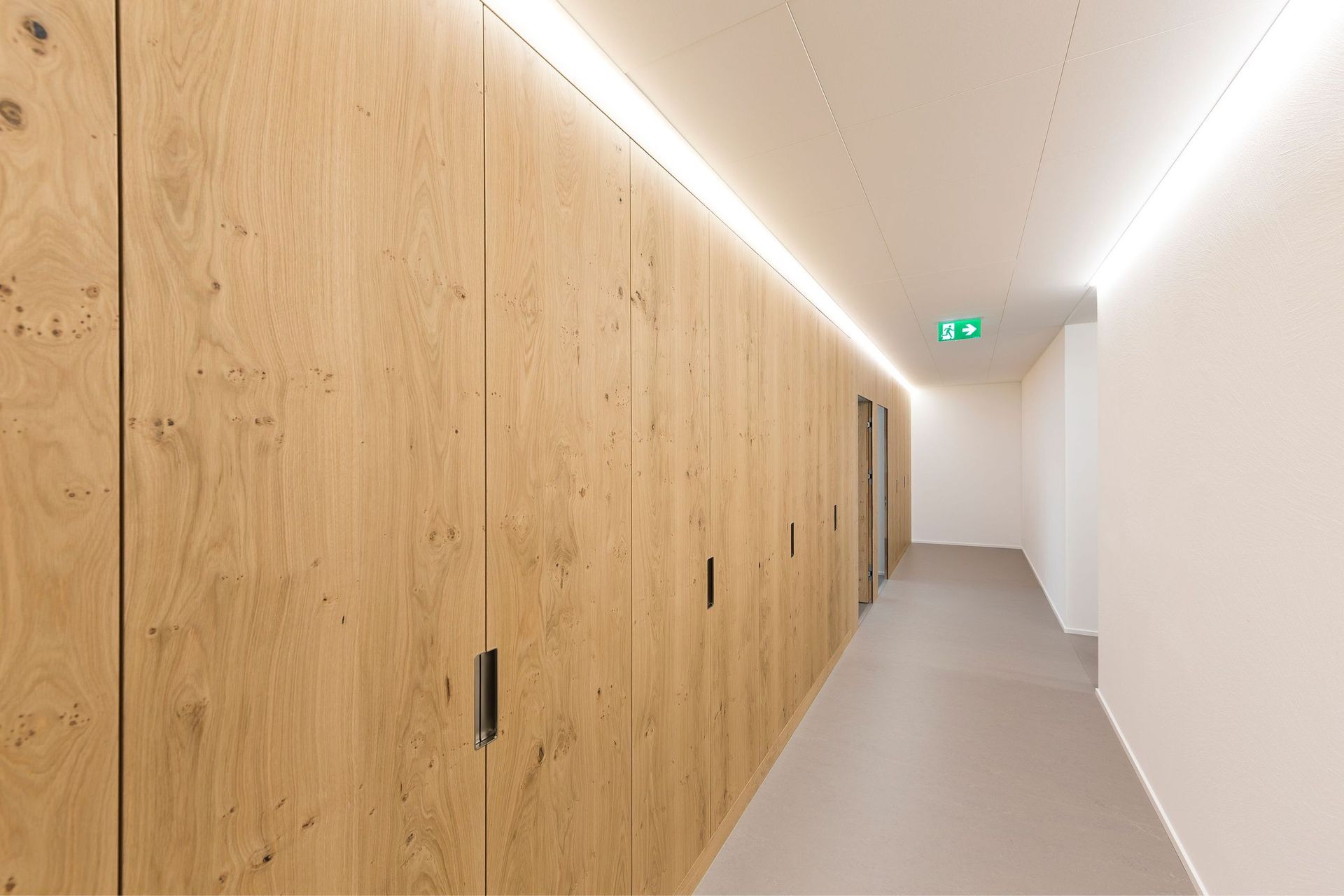 Ein langer Flur mit Holzschränken und einem grünen Ausgangsschild.