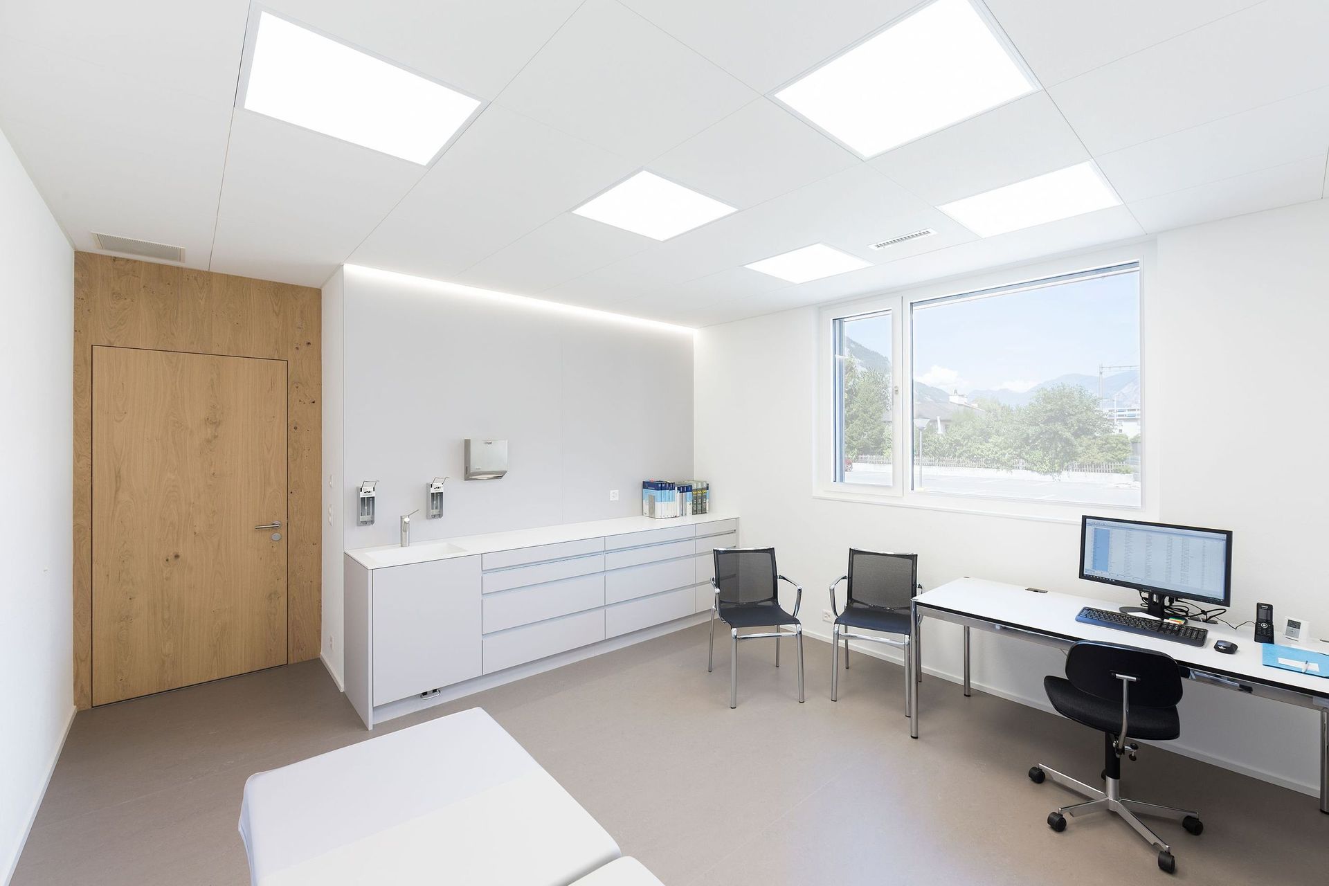 Eine Arztpraxis mit Schreibtisch, Stühlen und einem Computer.