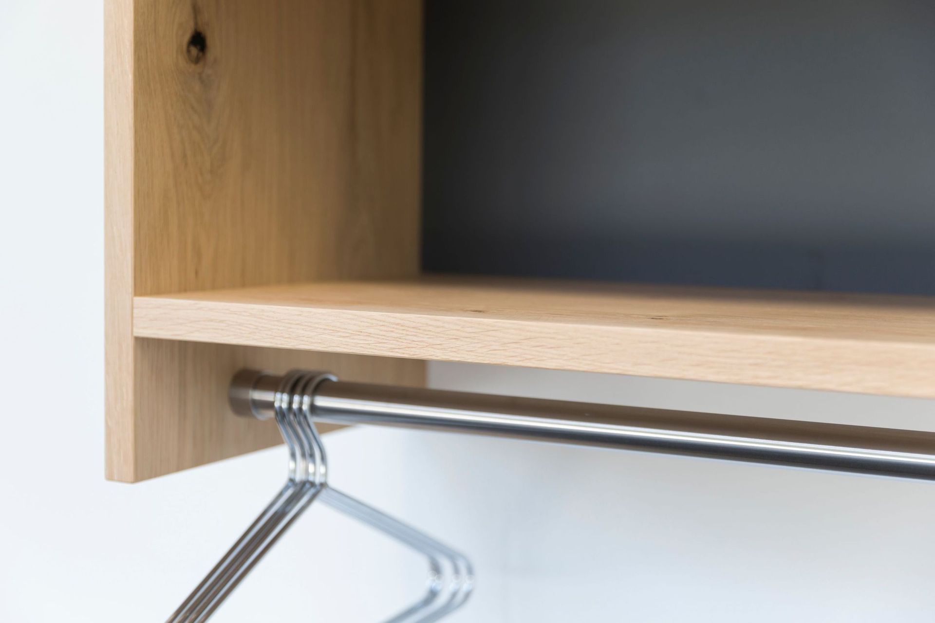 Ein Holzregal, an dem ein Kleiderbügel aus Metall hängt.