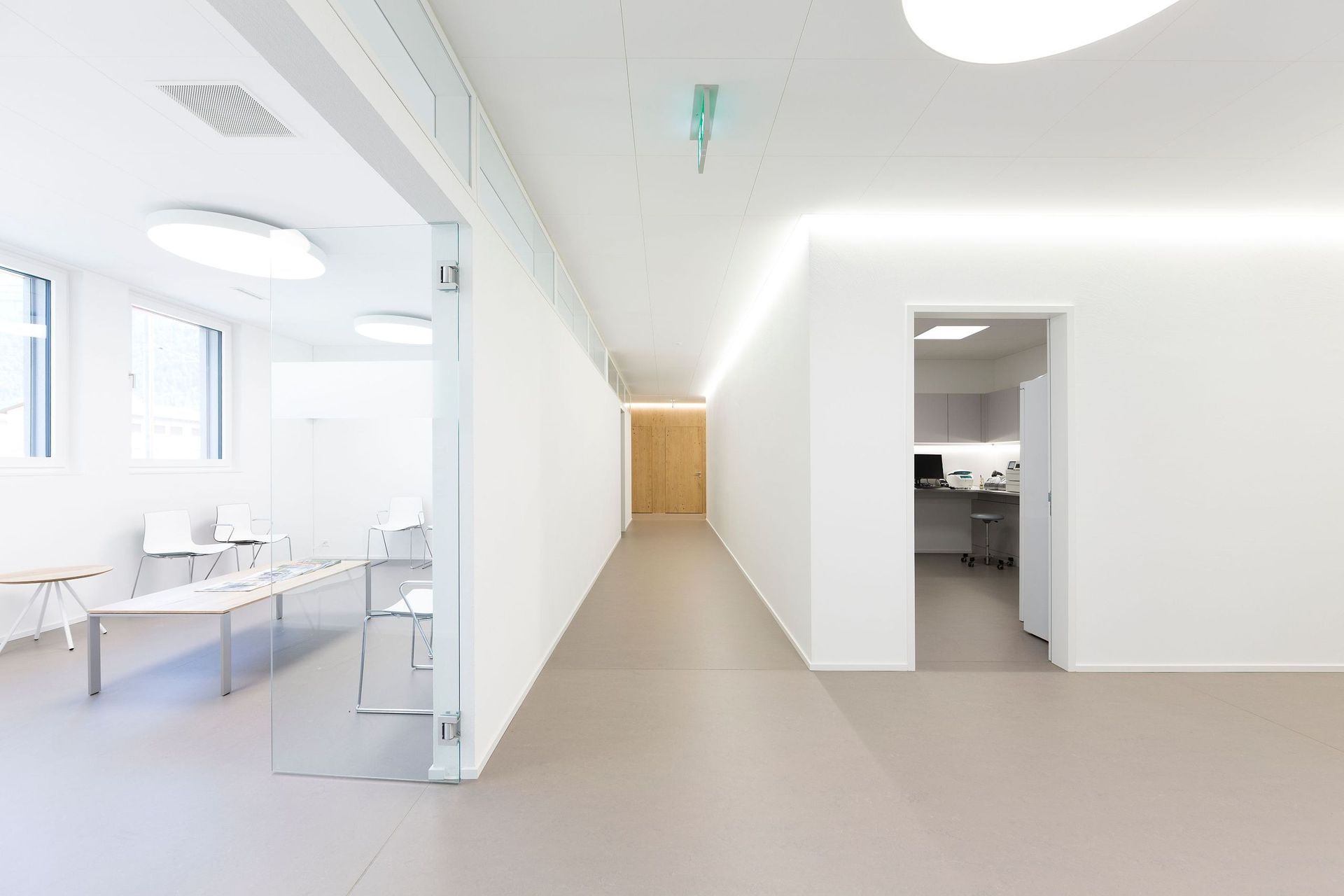 Ein langer weißer Flur mit einer Glastür, die zu einem Wartezimmer führt.