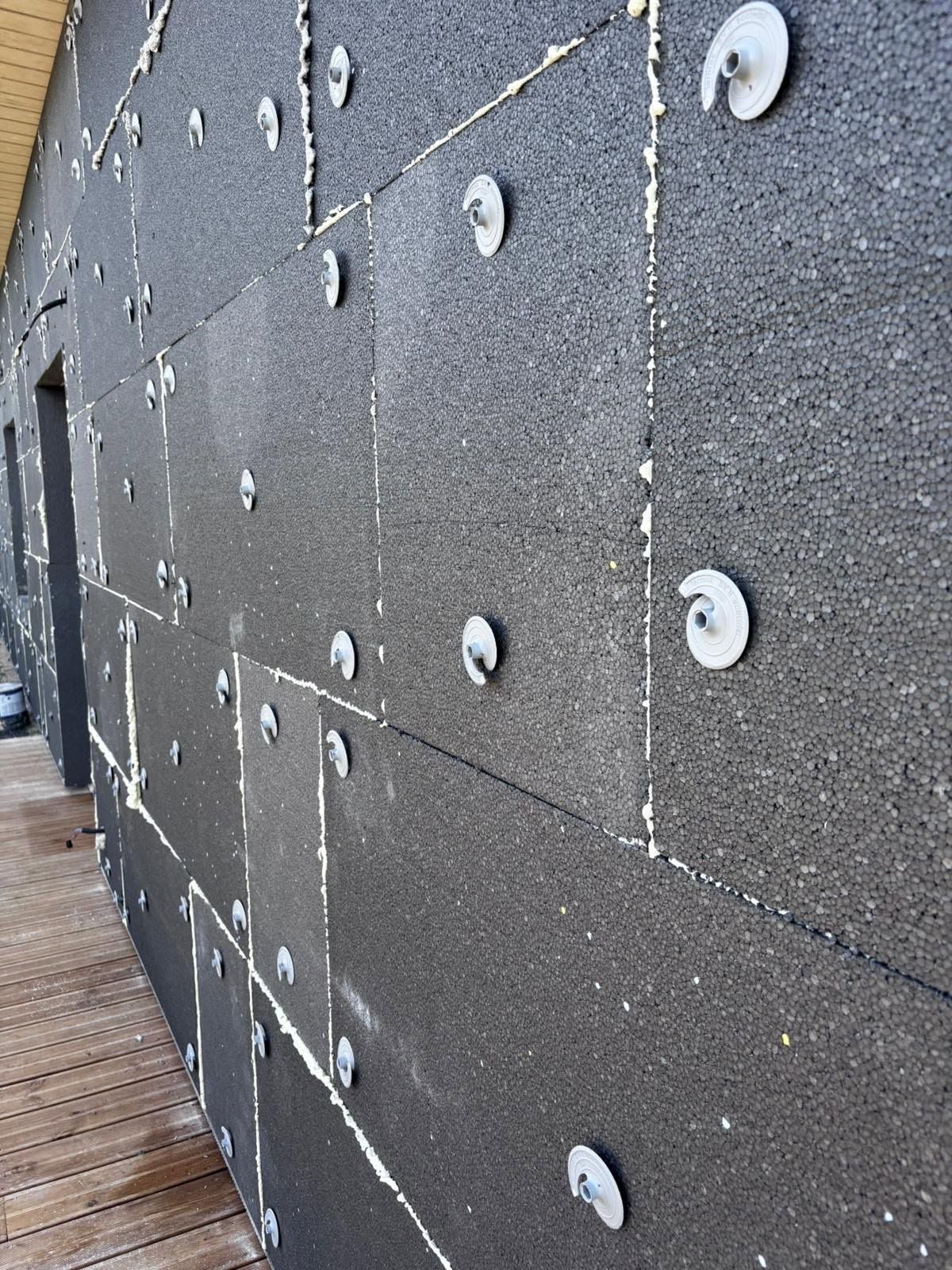 Panneaux muraux d'isolation gris foncé avec fixations blanches, le long d'une terrasse en bois.