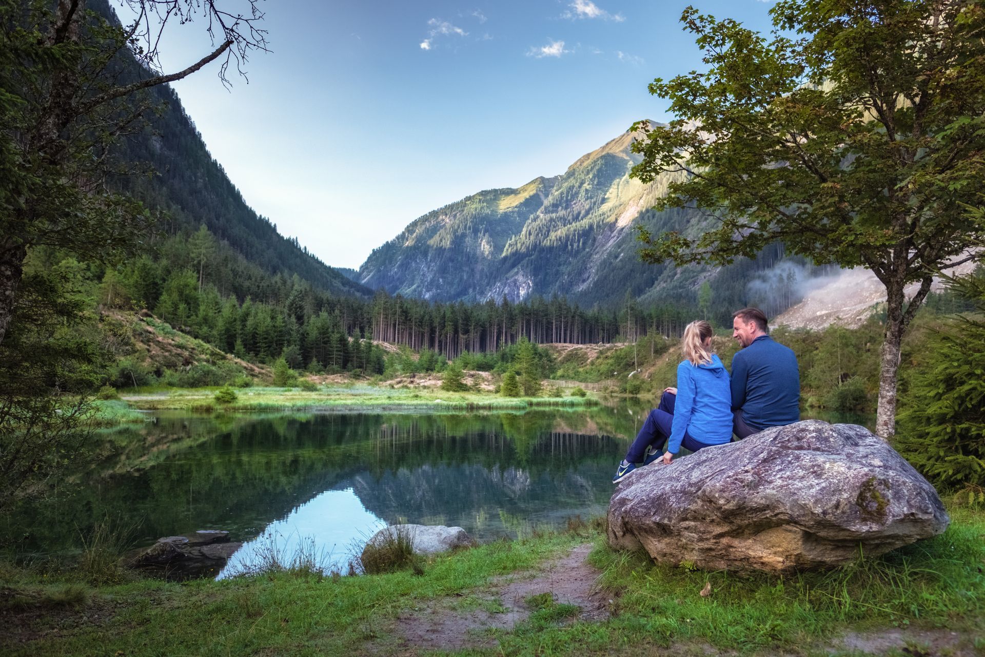 Ein Mann und eine Frau sitzen auf einem Felsen in der Nähe eines Sees.