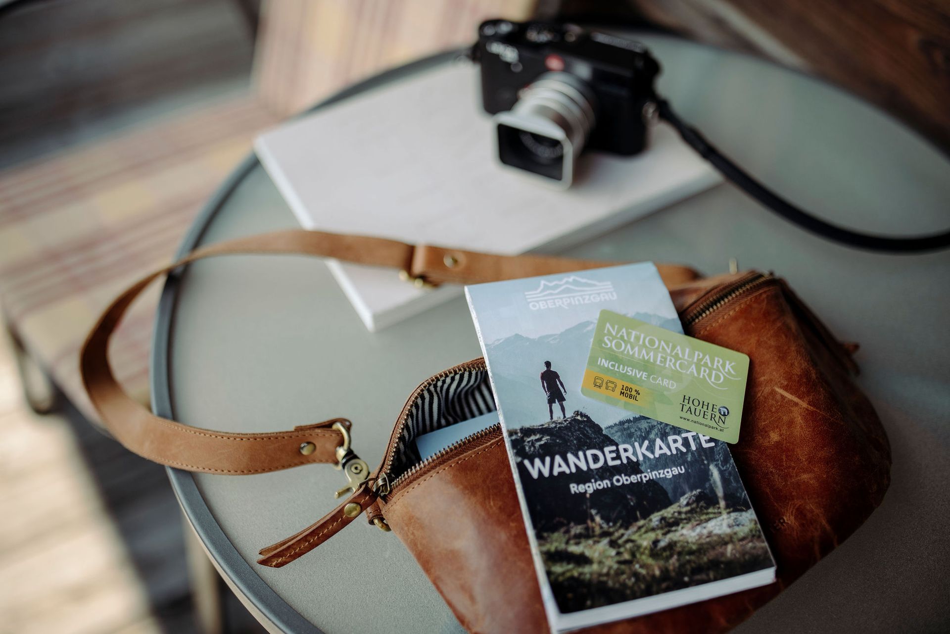 Ein Wanderkartenbuch liegt neben einer Kamera auf einem Tisch.