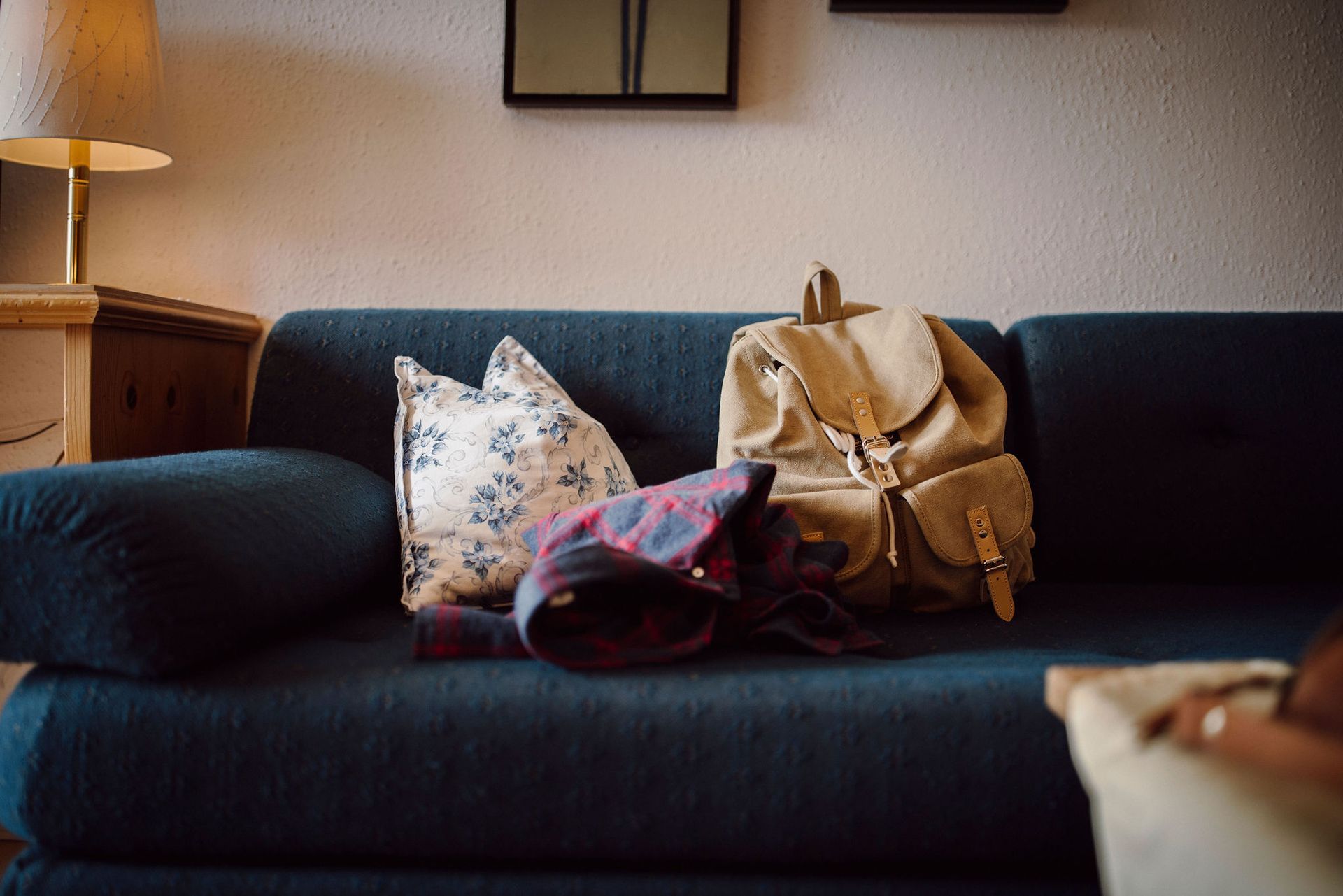 Eine Couch mit einem Rucksack und Kissen darauf in einem Wohnzimmer.