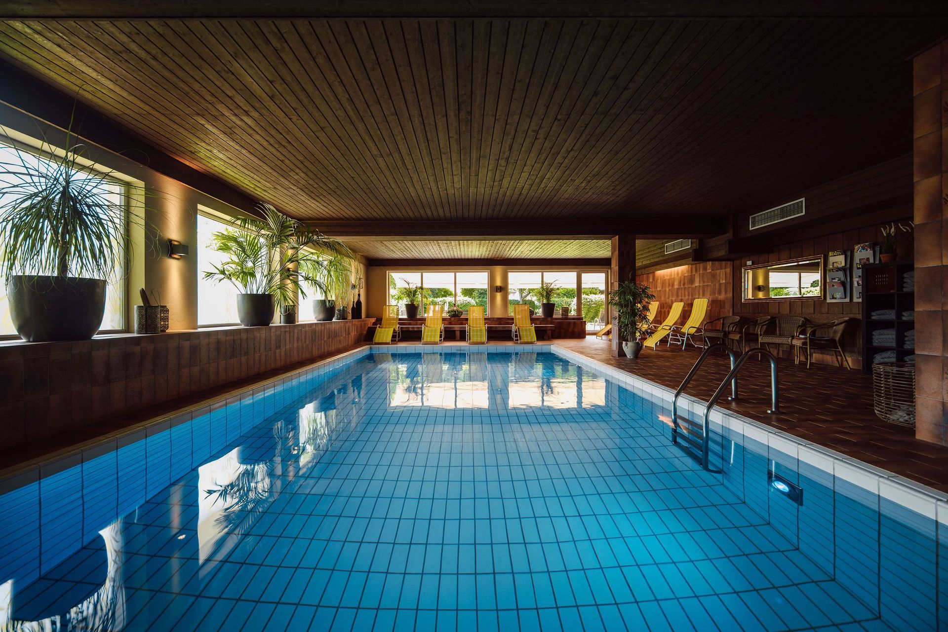 Ein großes Hallenbad mit vielen Fenstern und Stühlen drumherum.