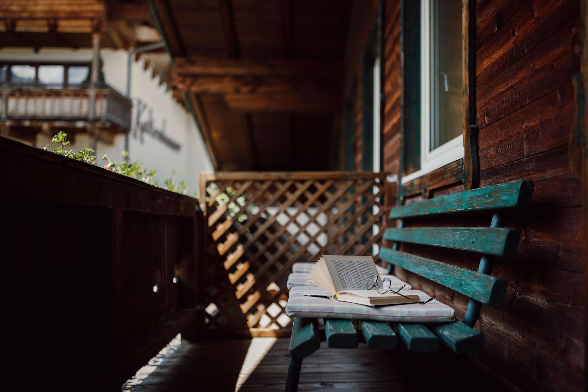 Auf einer Holzveranda steht eine Holzbank mit einem Buch darauf.