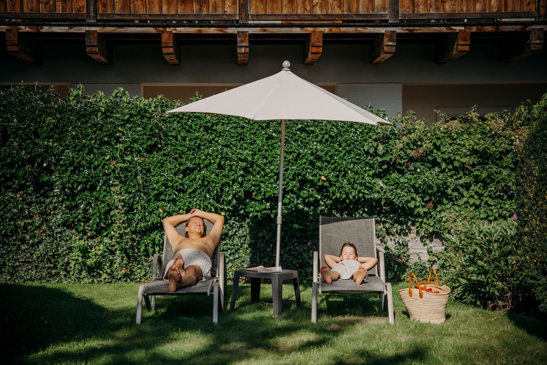 Ein Mann und ein Kind liegen in Liegestühlen unter einem Sonnenschirm.