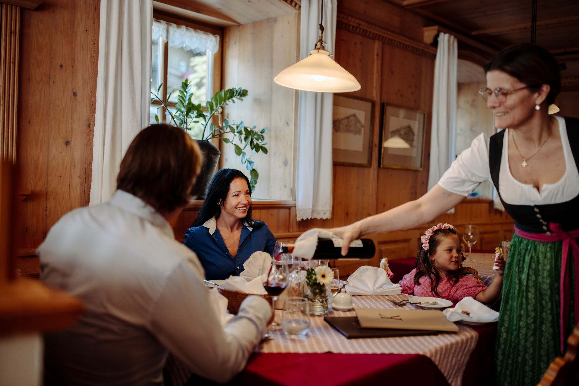Eine Frau serviert einer Familie, die in einem Restaurant an einem Tisch sitzt, ein Glas Wein.