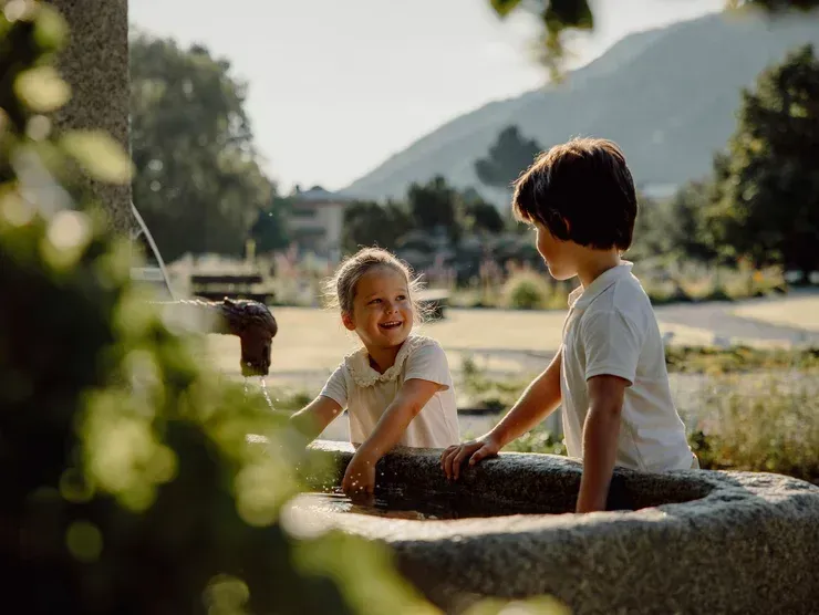 Ein Junge und ein Mädchen sitzen neben einem Brunnen.
