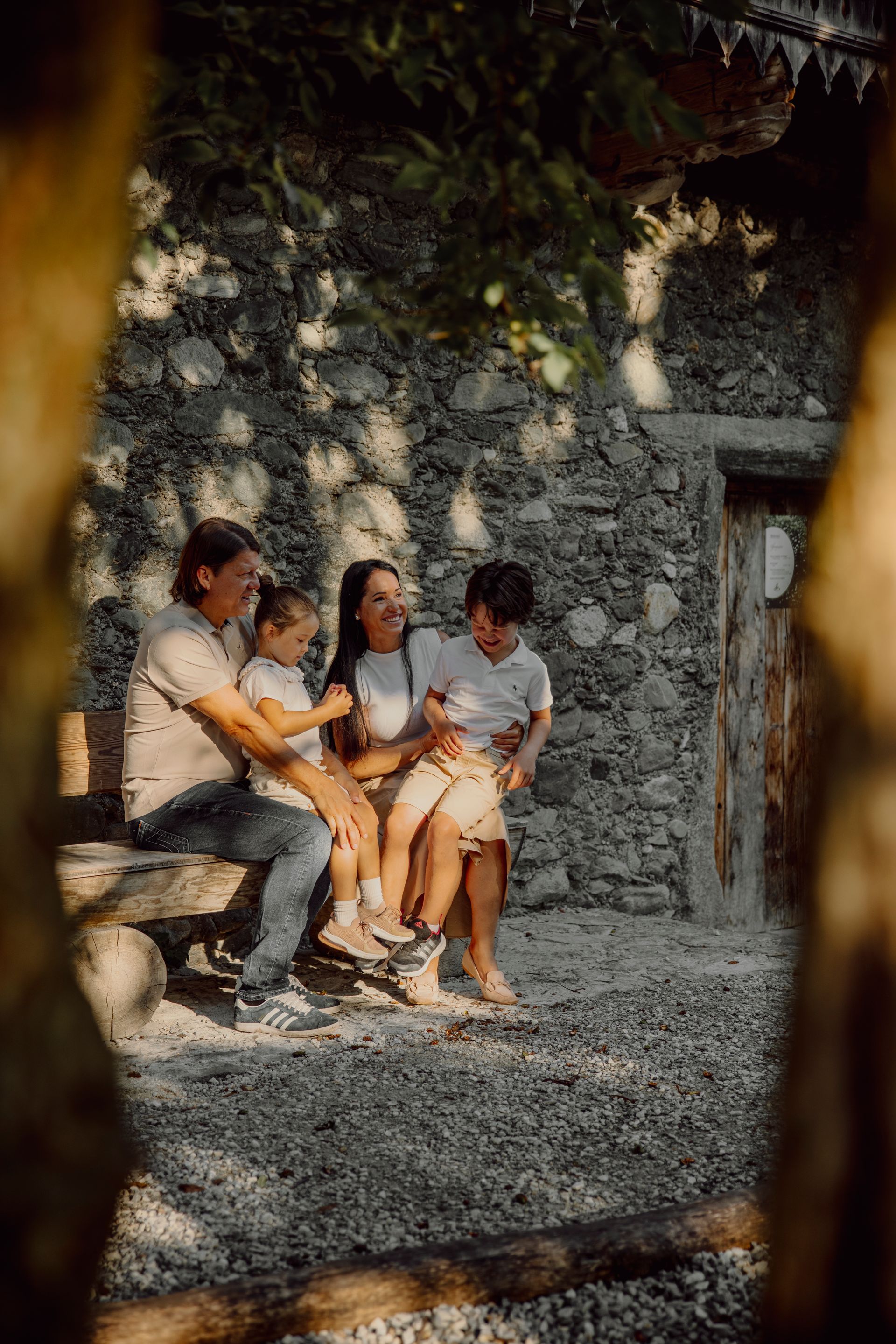 Eine Familie sitzt auf einer Bank vor einer Steinmauer.