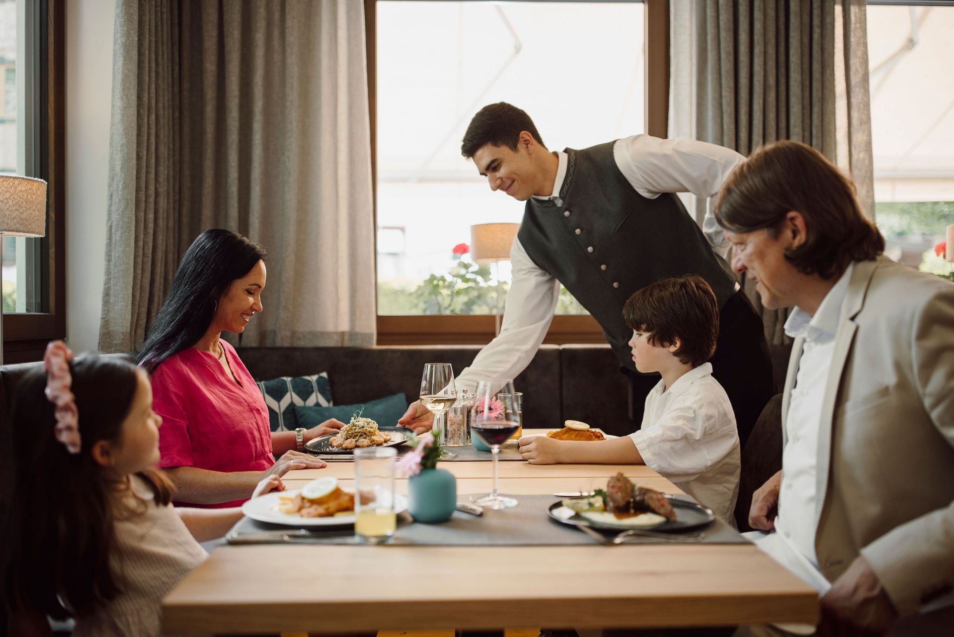 Eine Familie sitzt in einem Restaurant an einem Tisch, während ein Kellner ihnen Essen serviert.