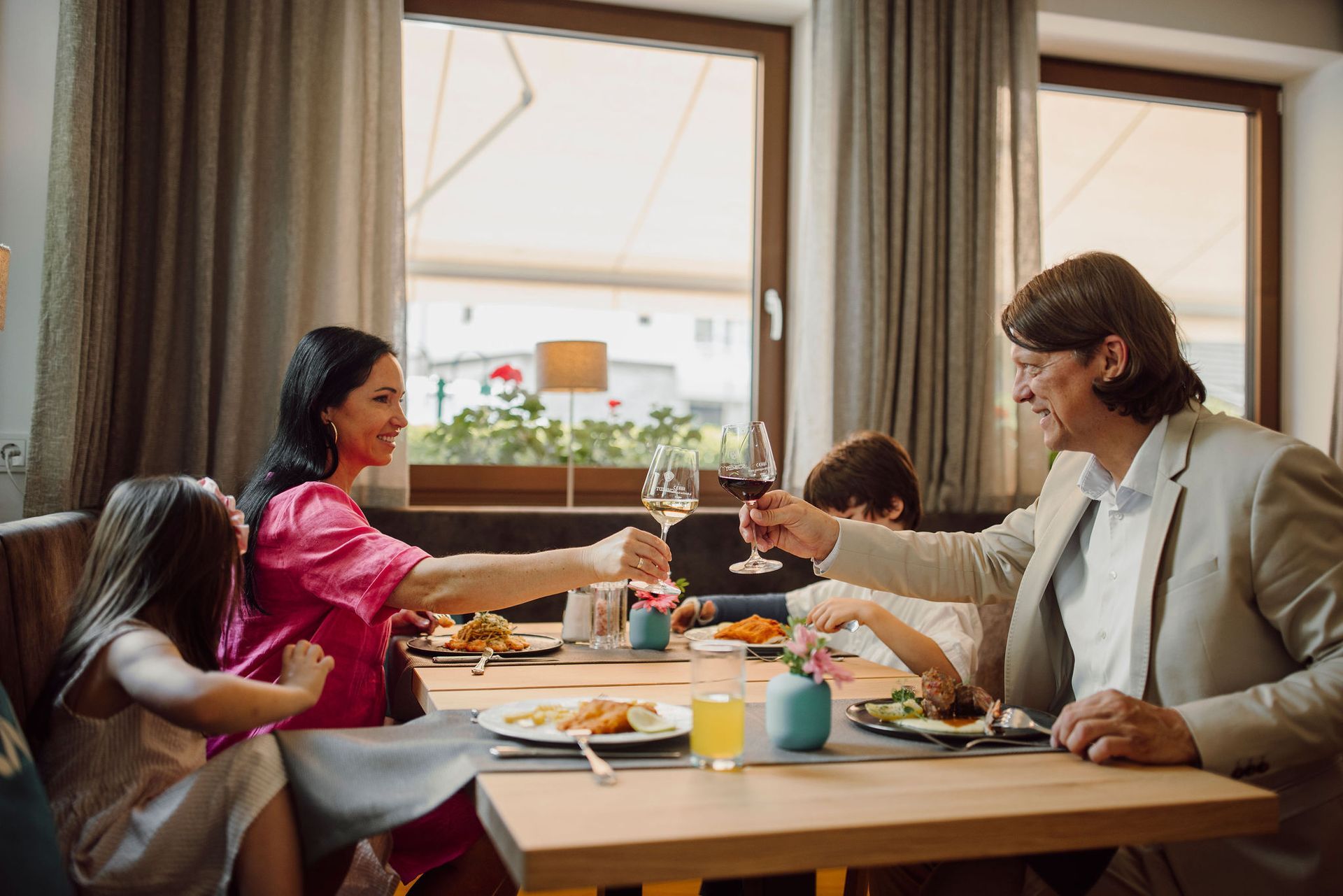 Eine Familie sitzt in einem Restaurant an einem Tisch und stößt mit Weingläsern an.