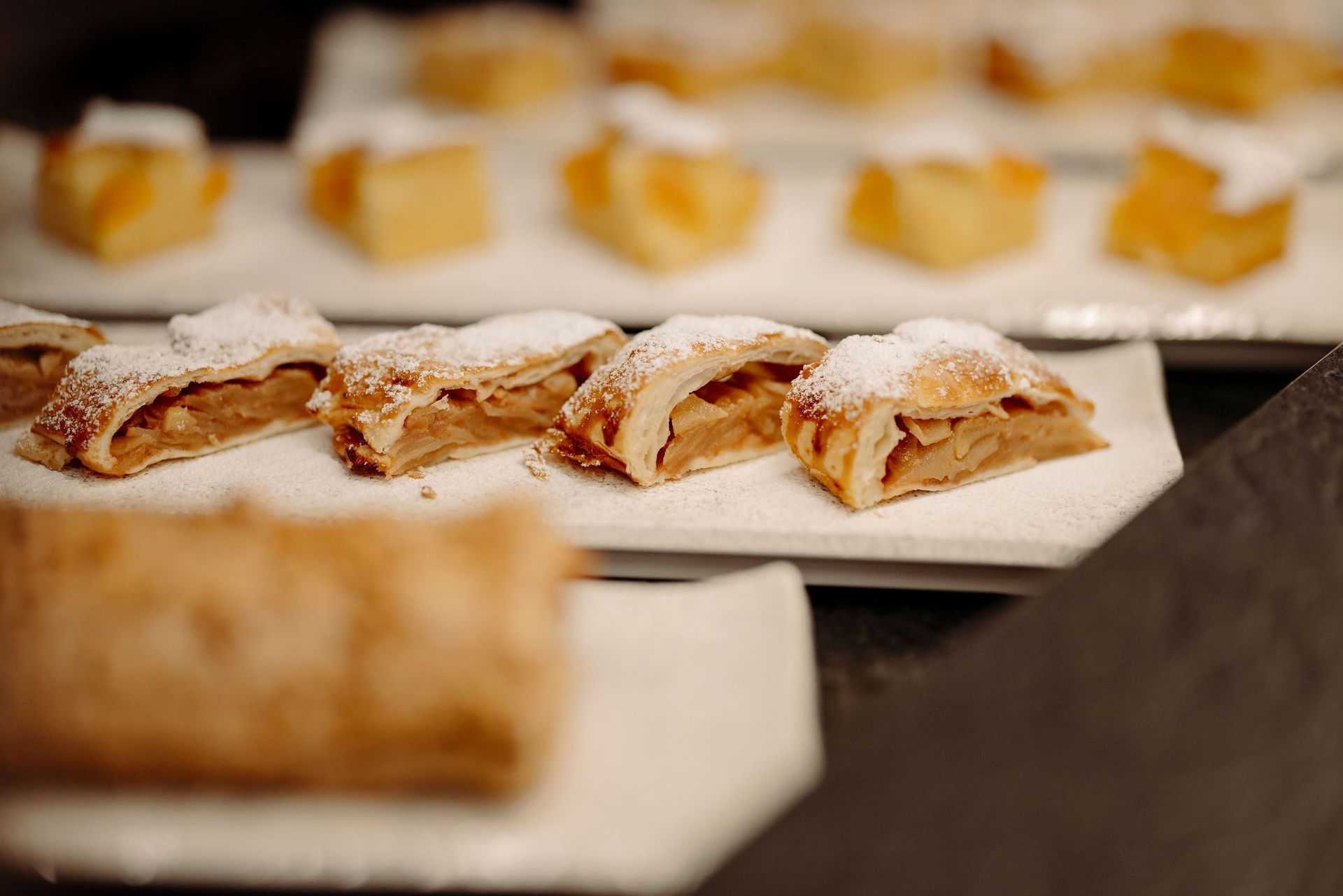 Eine Reihe mit Puderzucker bestäubter Apfelstrudel auf einem Tisch.